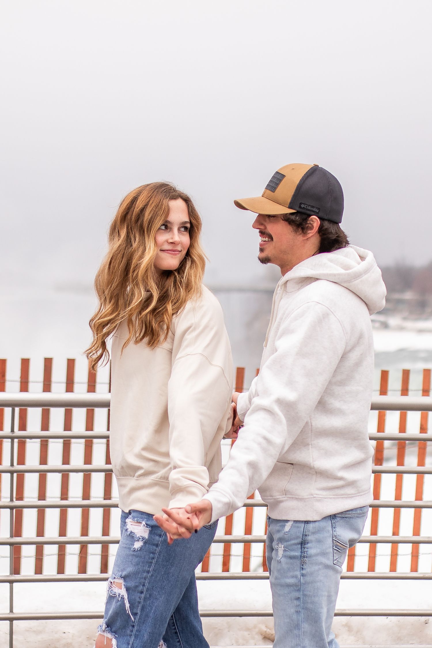 Newly engaged couple hold hands in front of Niagara Falls, New York after the surprise proposal during their engagement session.