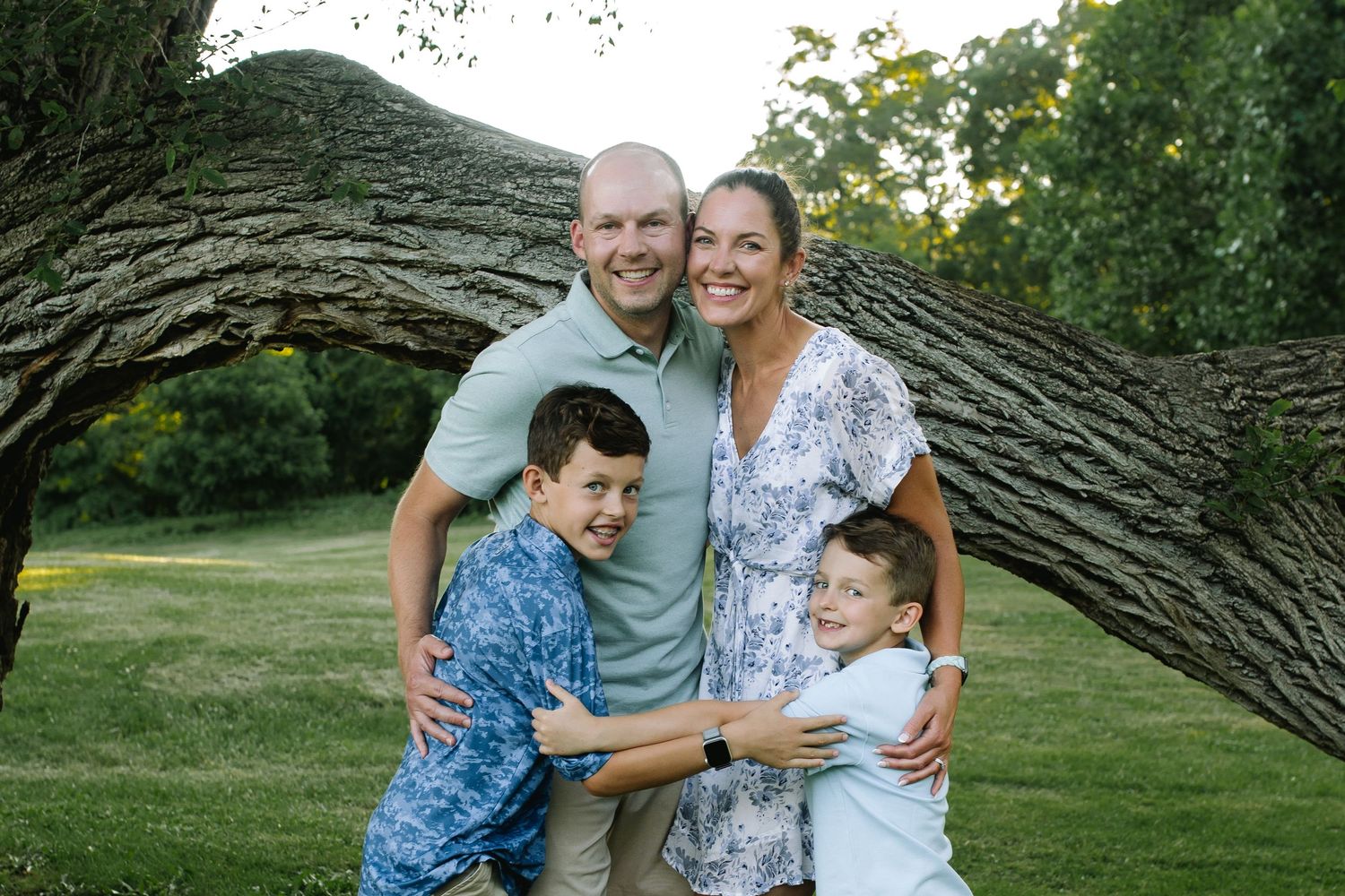 Parents and two young children embrace at the park at bond lake in Niagara county during their family session.