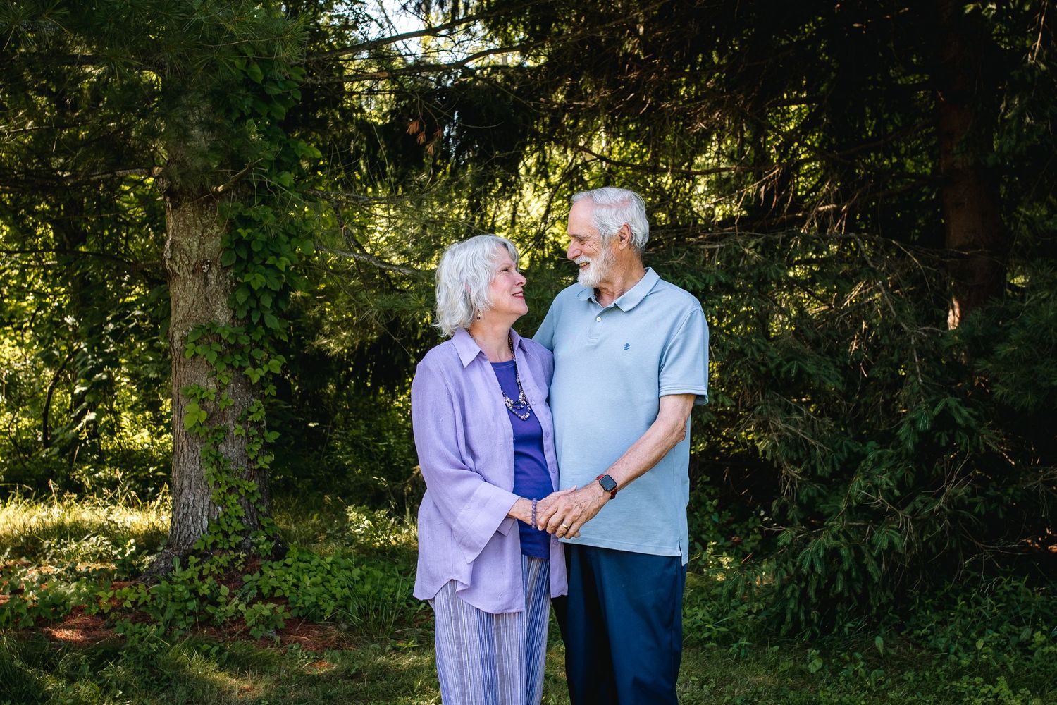 Older married couple hold hands at look at each other in a park in niagara county during their family portrait session