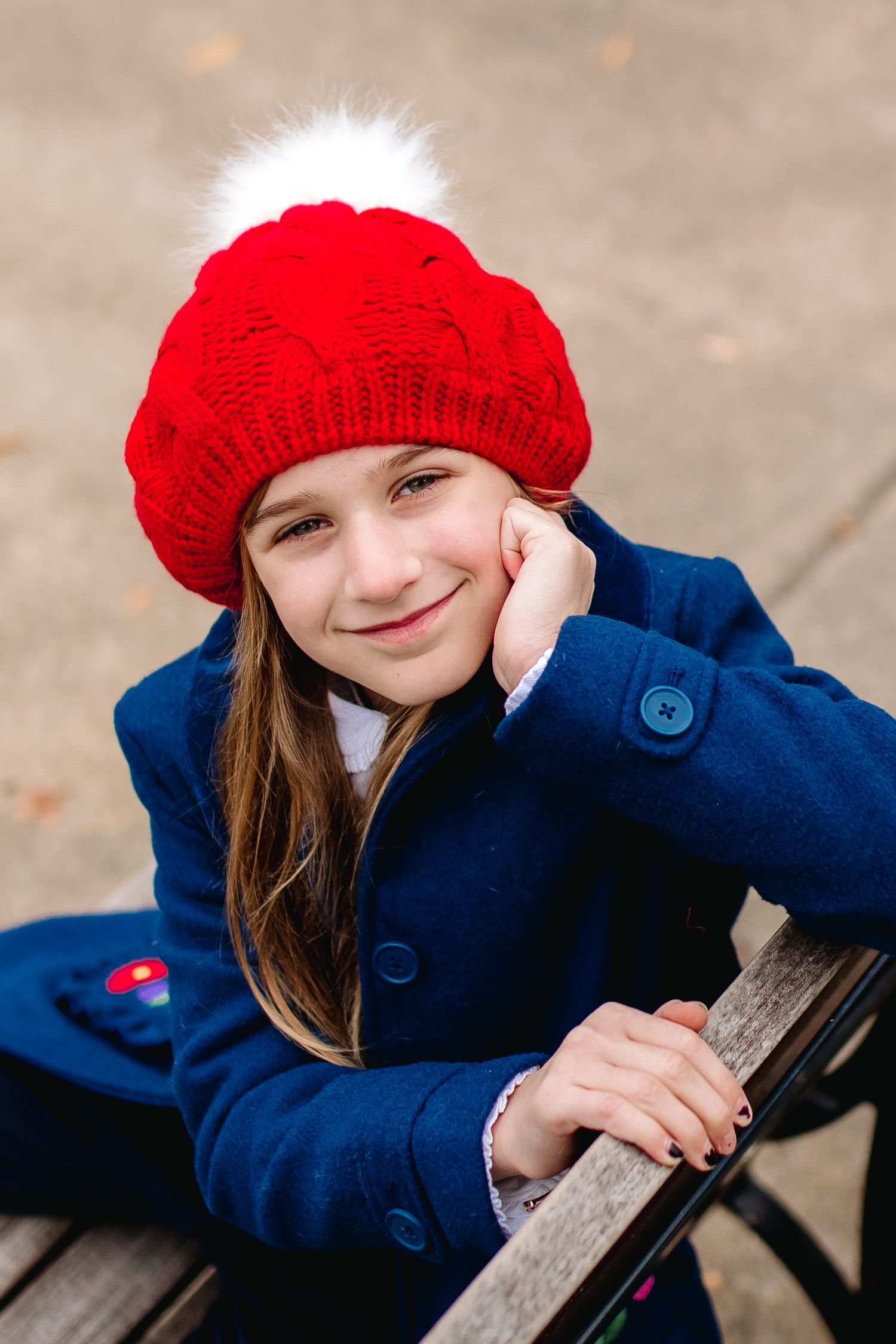 Young girl poses in red winter hat on bench at delaware park in buffalo new york during her fall family portrait session
