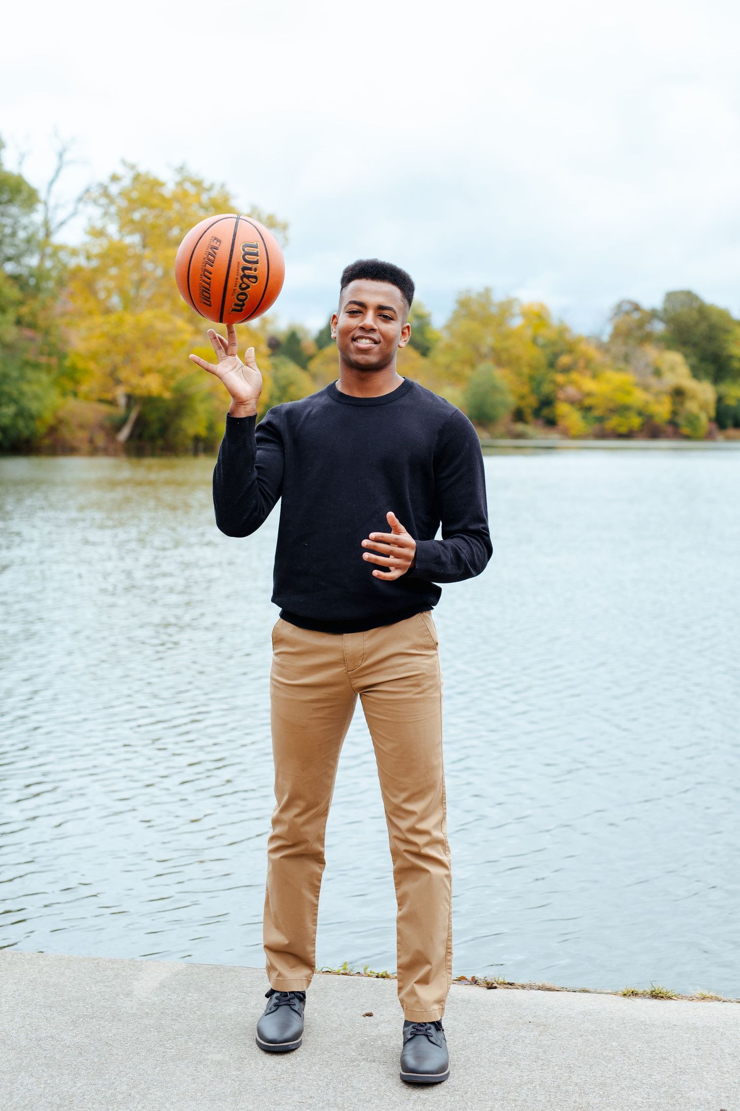 High School Senior Tommy poses by the water with his basketball at his senior session at hoyt lake in Delaware Park in Buffalo, New York.