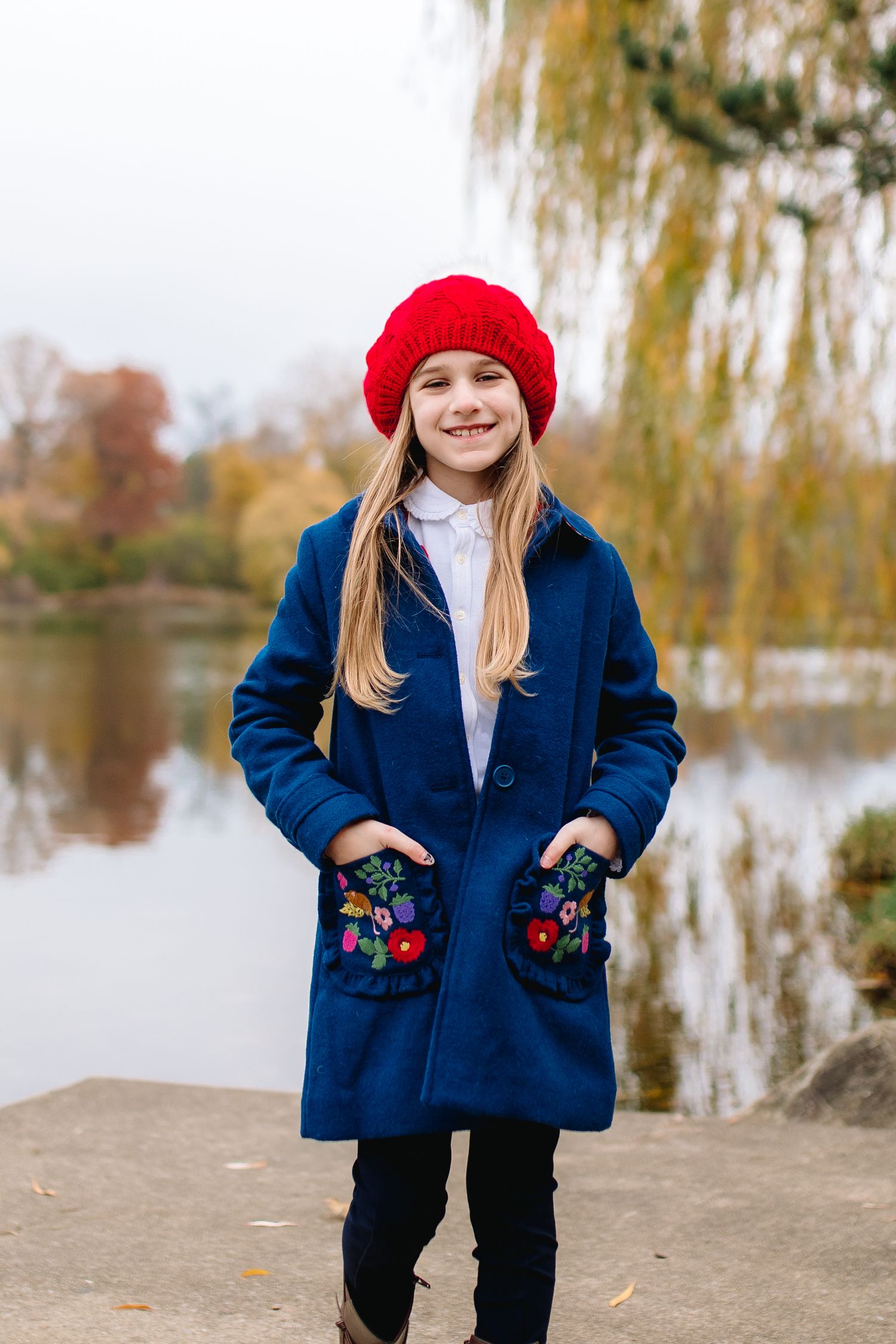 Young girl poses in red winter hat on bench at delaware park in buffalo new york during her fall family portrait session