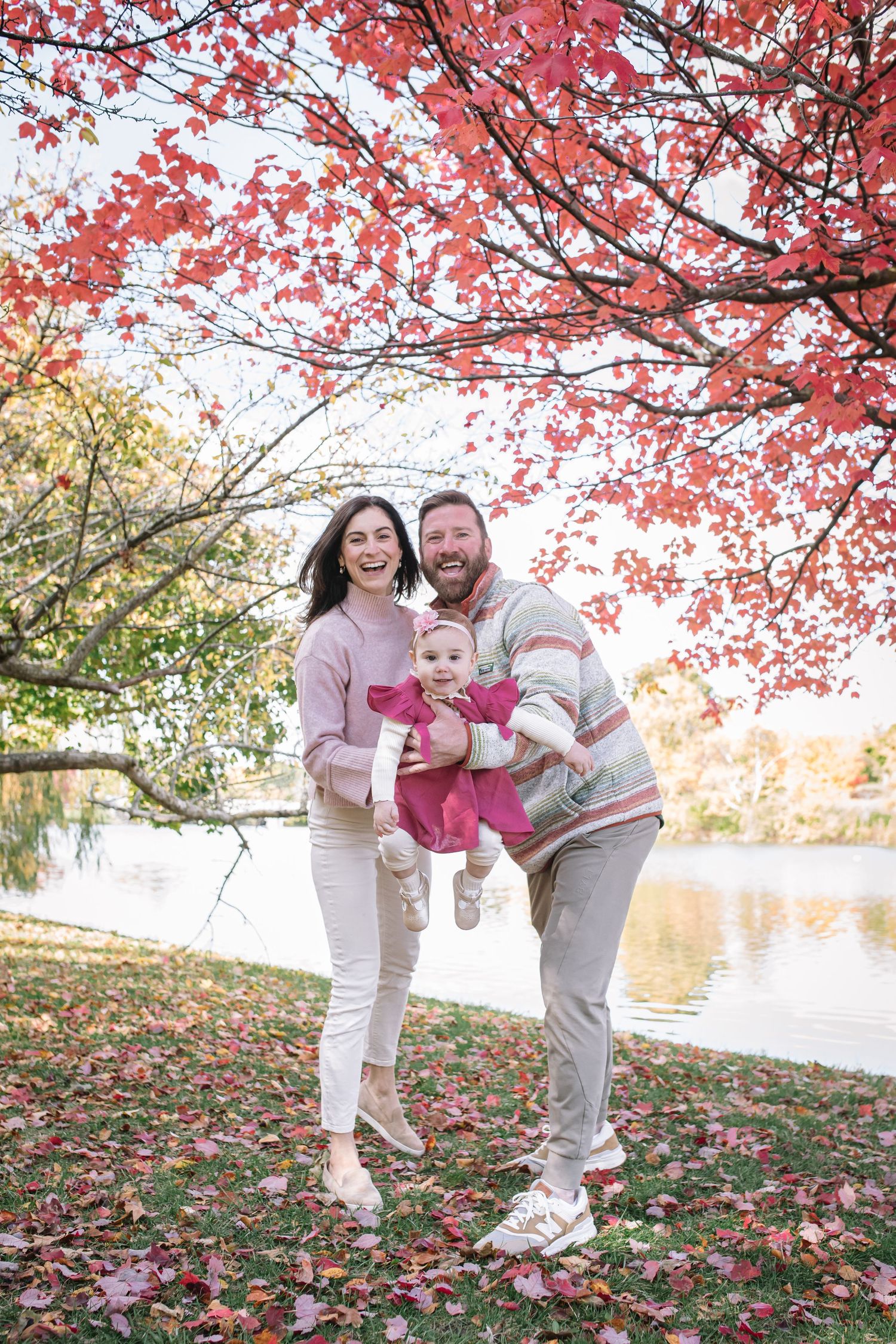 Family of three play under trees at Delaware Park at Hoyt Lake in Buffalo New York during their fall family session