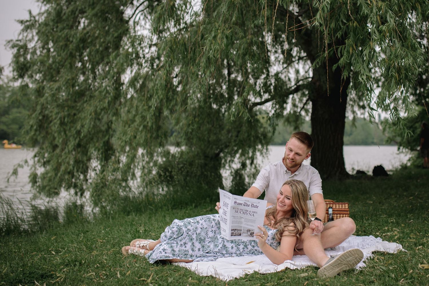 A couple enjoys a romantic picnic under willow trees by Hoyt Lake in Delaware Park in Buffalo at their engagement session.