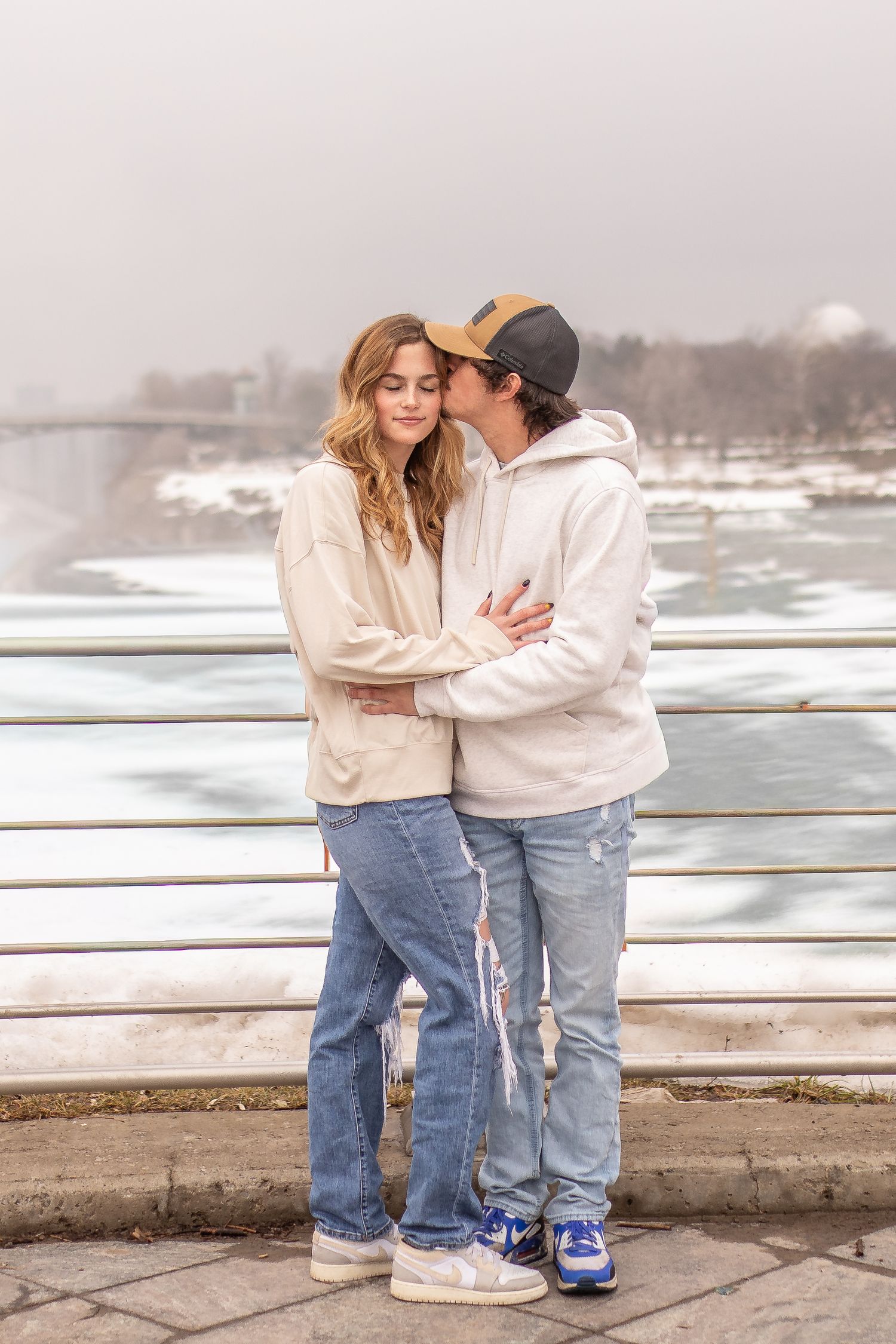 Newly engaged couple embrace in front of Niagara Falls, New York after the surprise proposal during their engagement session.