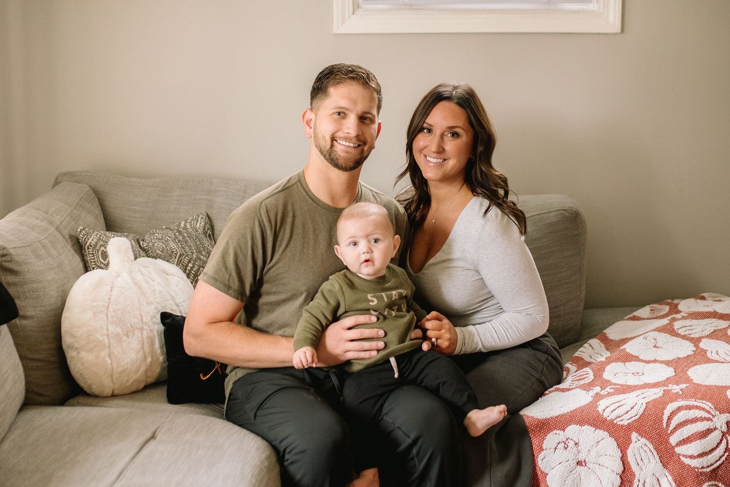 Mom, dad and baby pose on the couch at their lifestyle in home session.