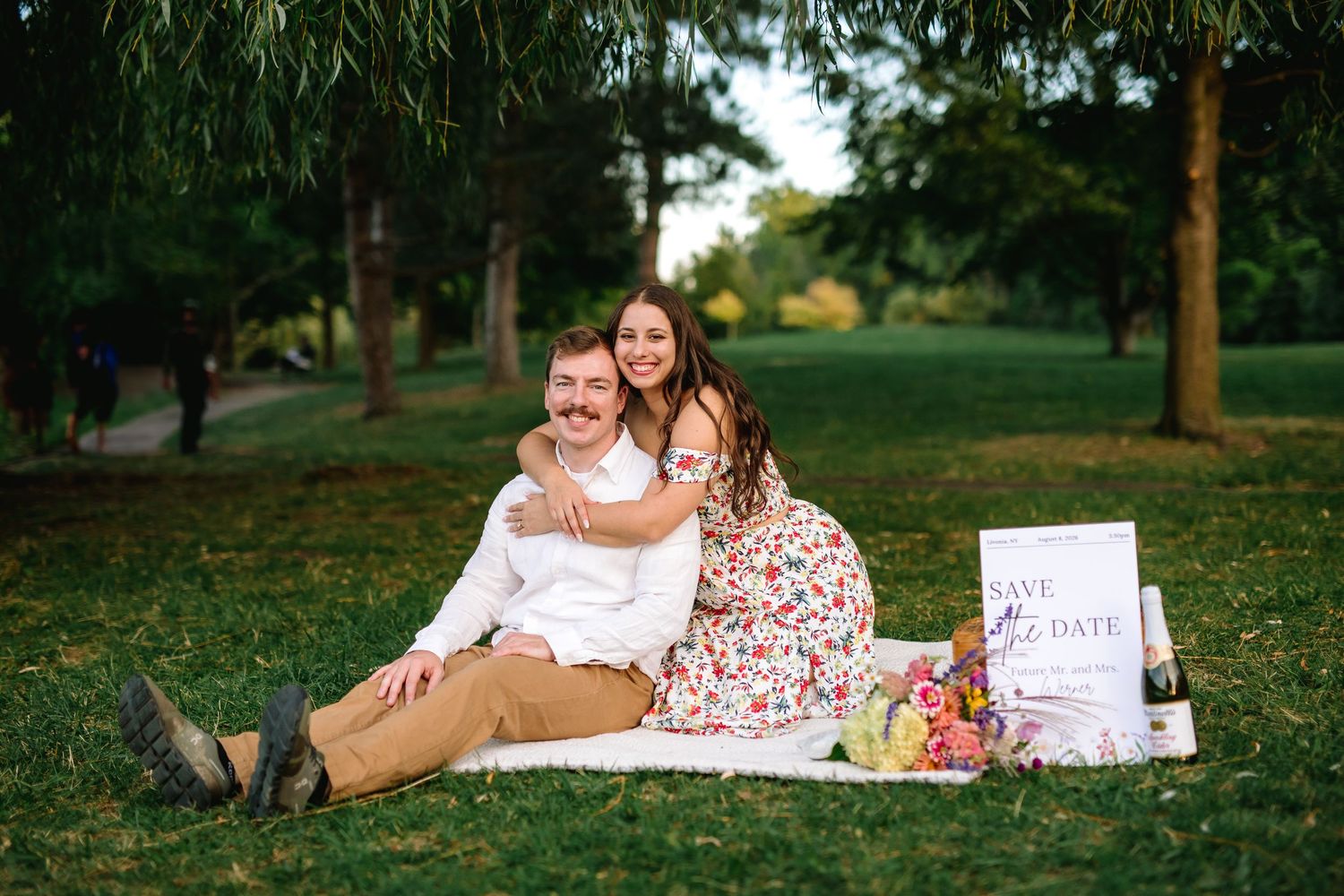 Newly engaged couple pose on a blanket surrounded by trees during their engagement session at Delaware Park in Buffalo, New York.