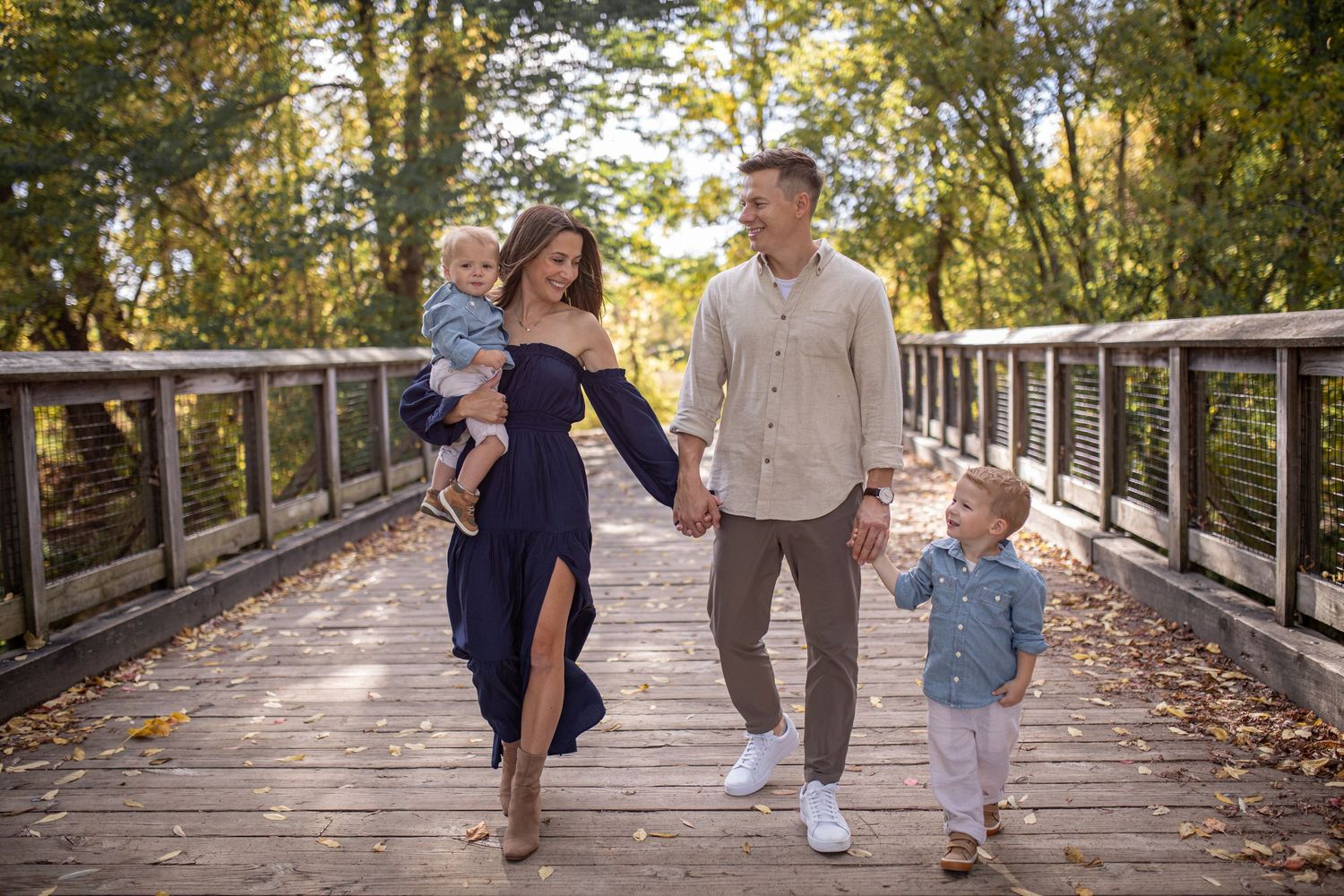 Mom, dad and two boys walk holding hands on a bridge at Amherst State Park in Buffalo, New York during their outdoor family sesion.