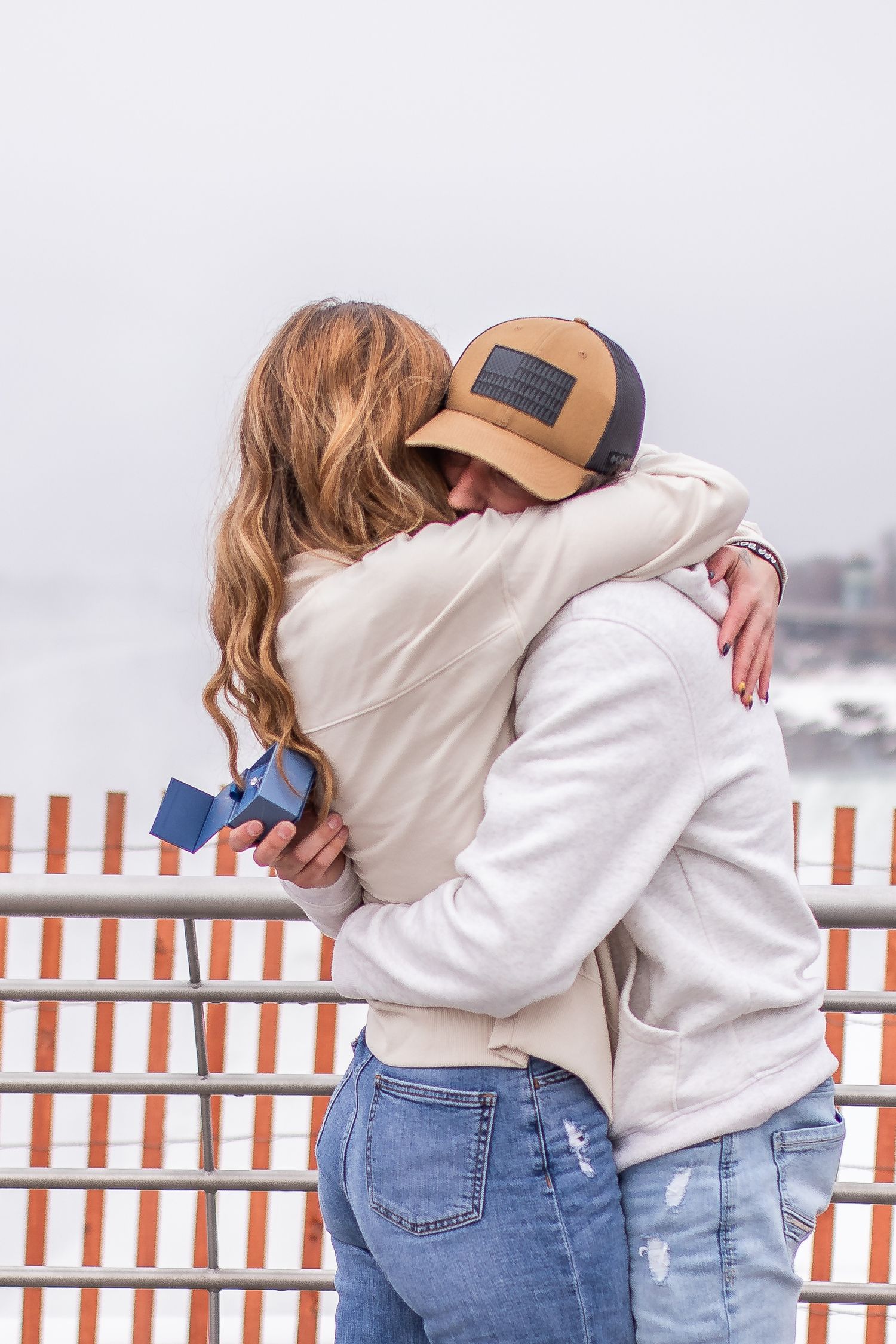 Newly engaged couple hug in front of Niagara Falls, New York after the surprise proposal during their engagement session.