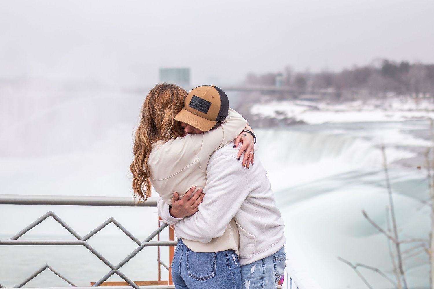 Newly engaged couple hug in front of Niagara Falls, New York after the surprise proposal during their engagement session.
