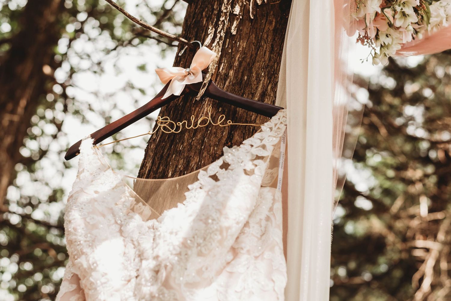 White wedding dress hanging outdoors against natural foliage and trees.