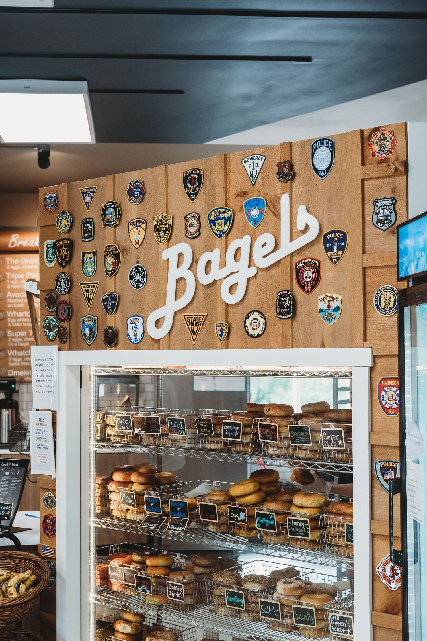 Bagel shop interior with wall decorated in police and security badges beneath vintage signage.