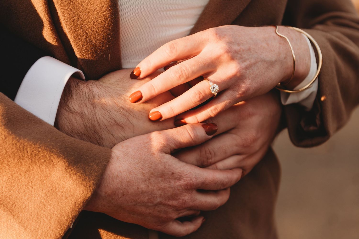 Close-up shot of hands tenderly touching against a warm brown background.