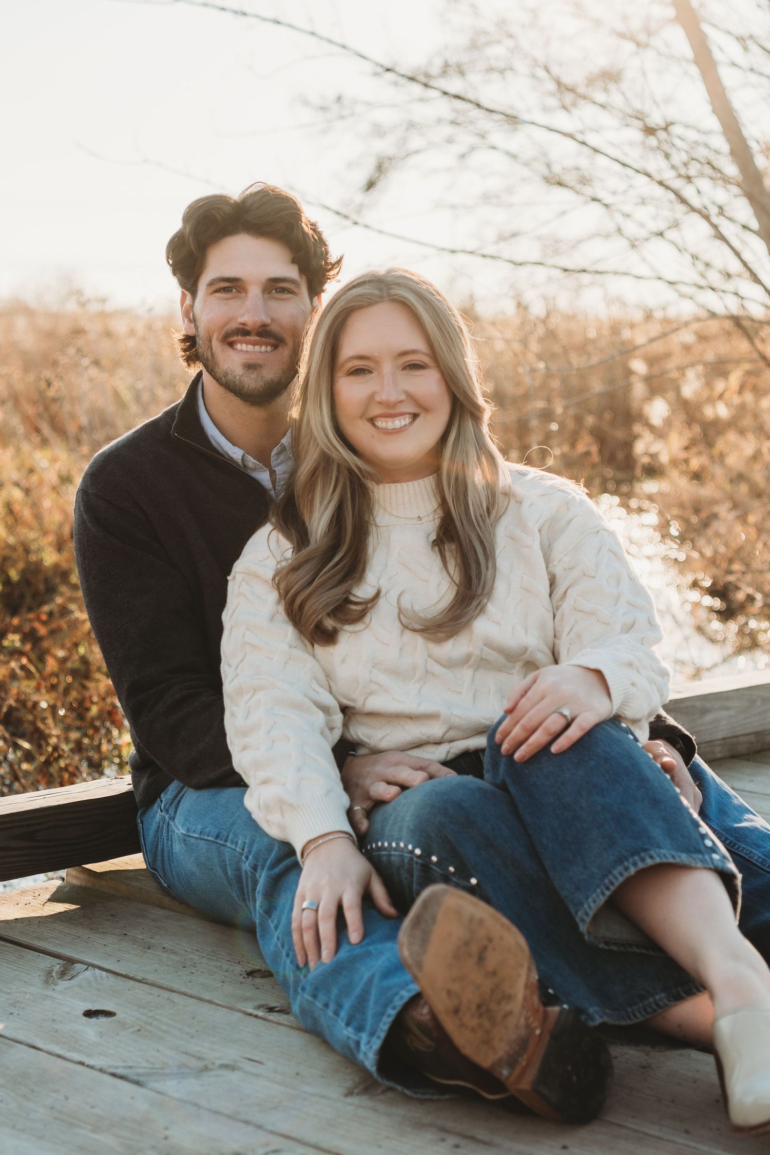 Couple sitting together outdoors on a wooden surface during a golden hour photoshoot.