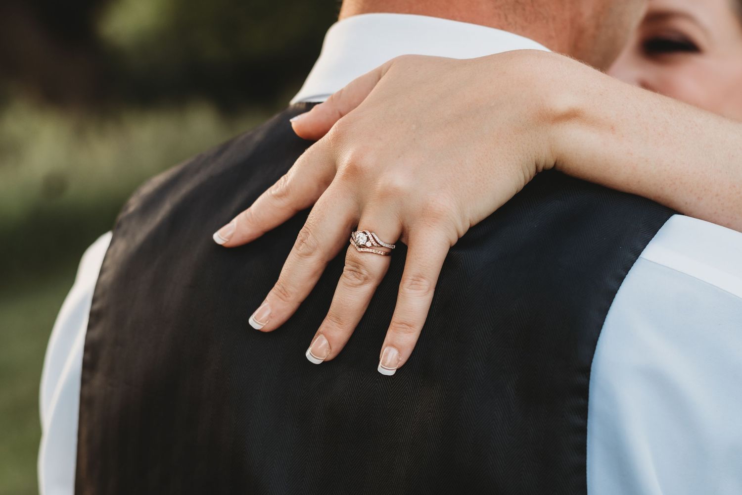 Close-up of engagement ring on hand against dark formal attire.