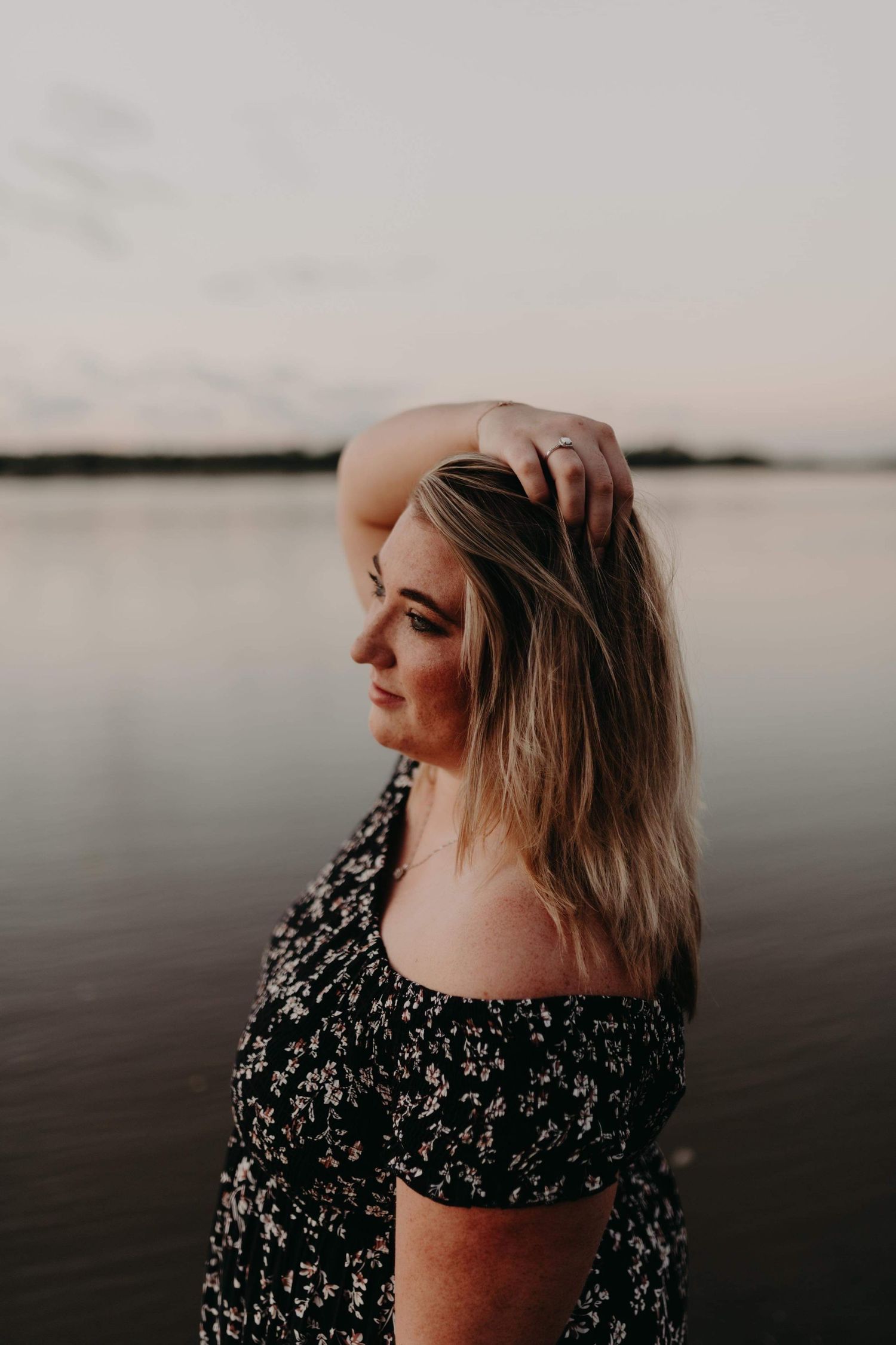 Silhouette of person in floral dress against sunset over water.
