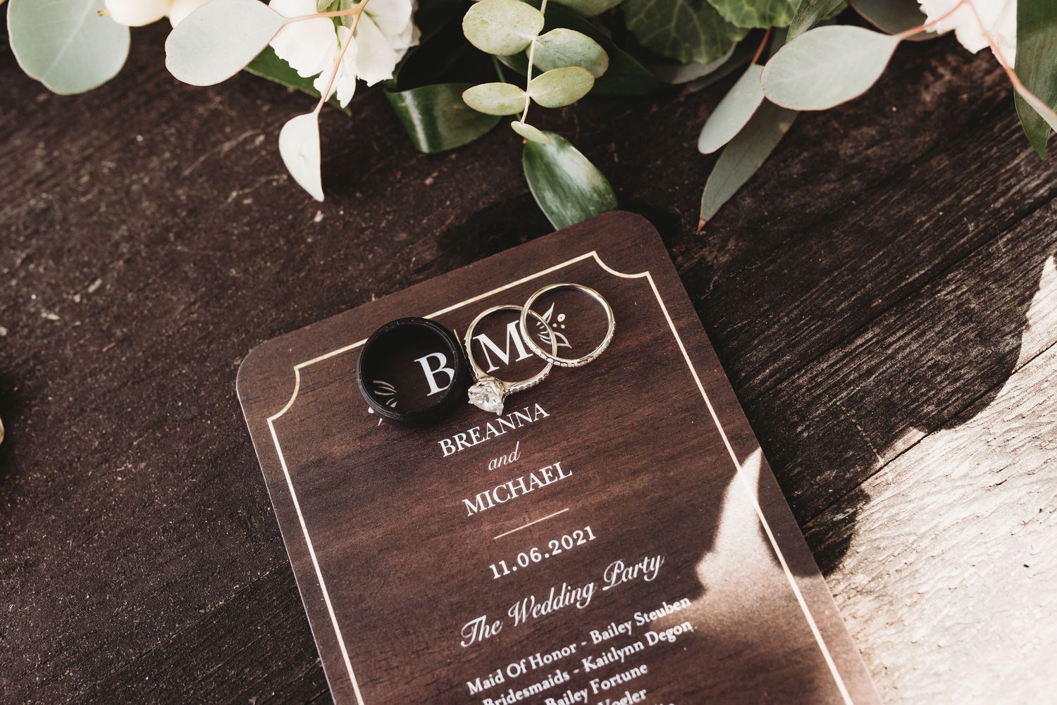 Wooden wedding invitation cards displayed with white roses and eucalyptus leaves.