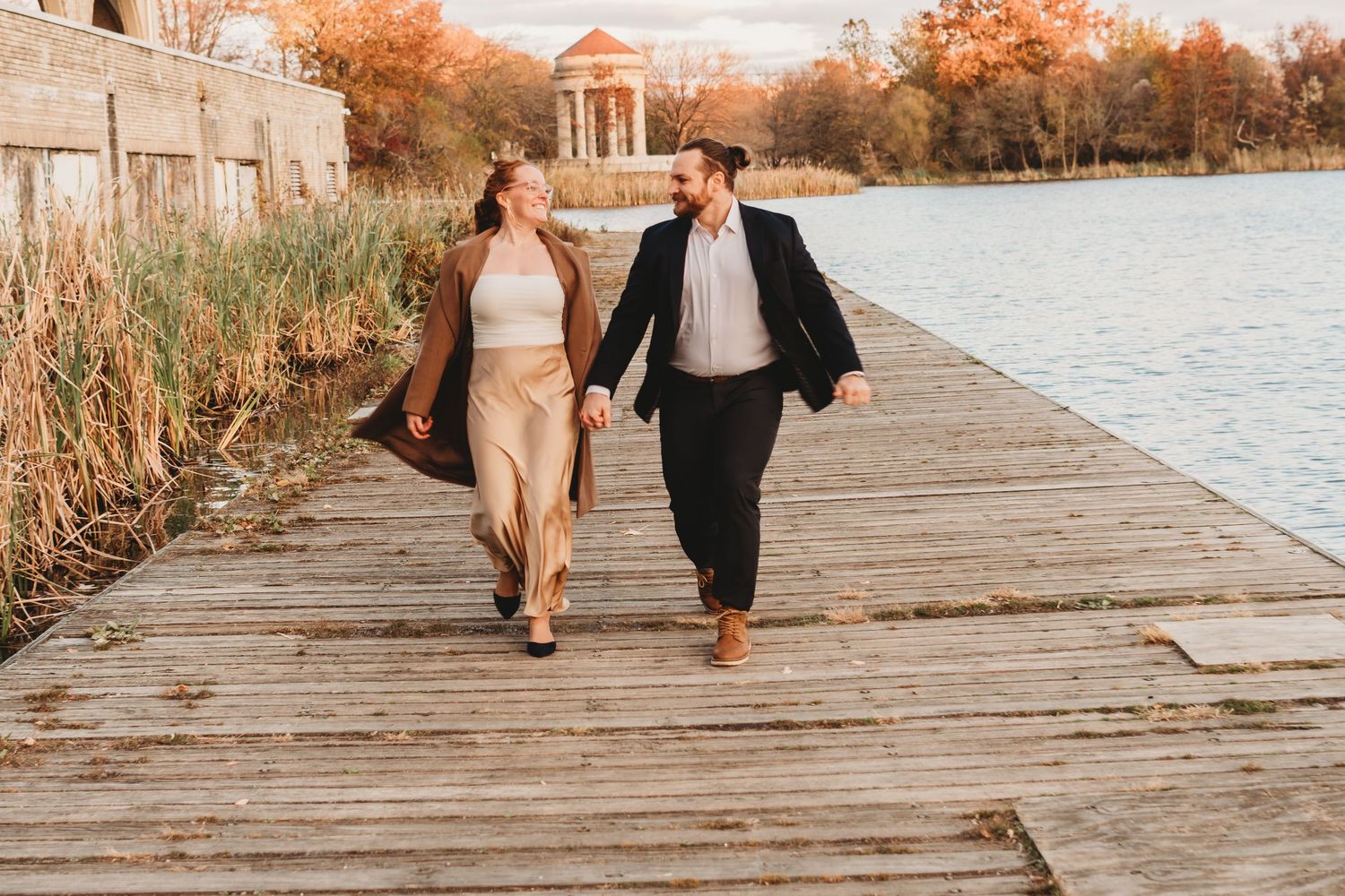 Couple walking along a wooden boardwalk by a lake during golden hour.