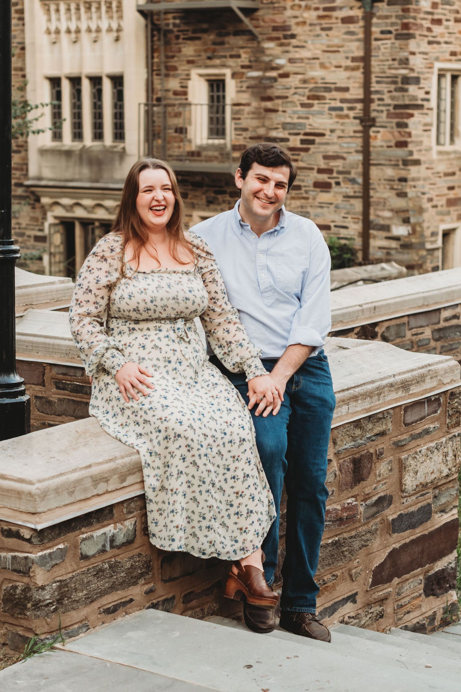 Couple sitting on stone steps of historic brick building sharing joyful moment.