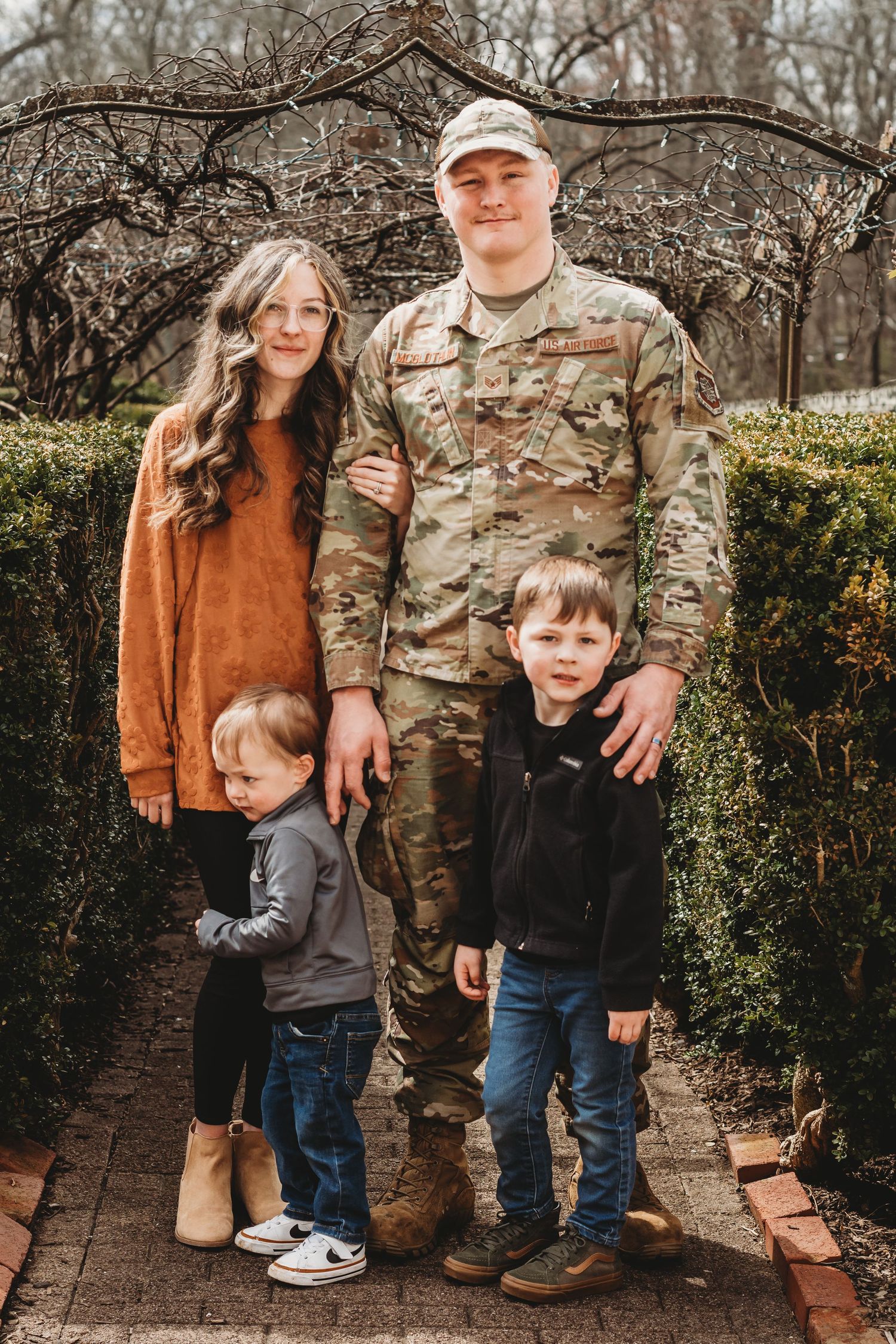 A series of outdoor family portraits taken against a stone wall and green hedge backdrop in casual and military attire.