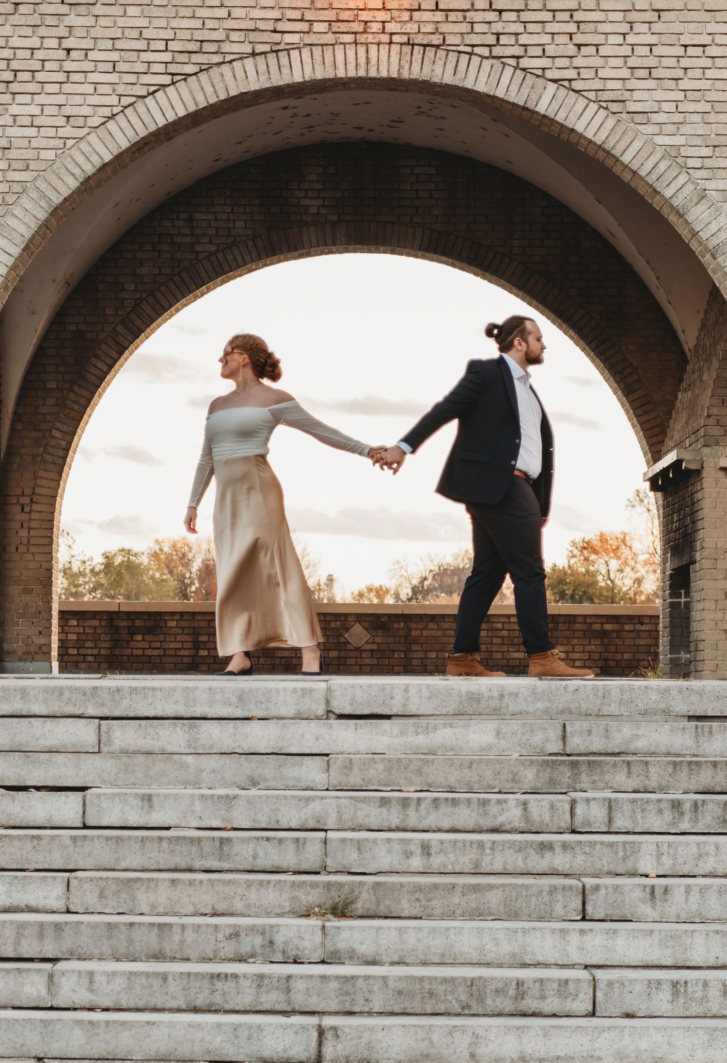 Playful sequence of couple ascending stone steps under brick archways.