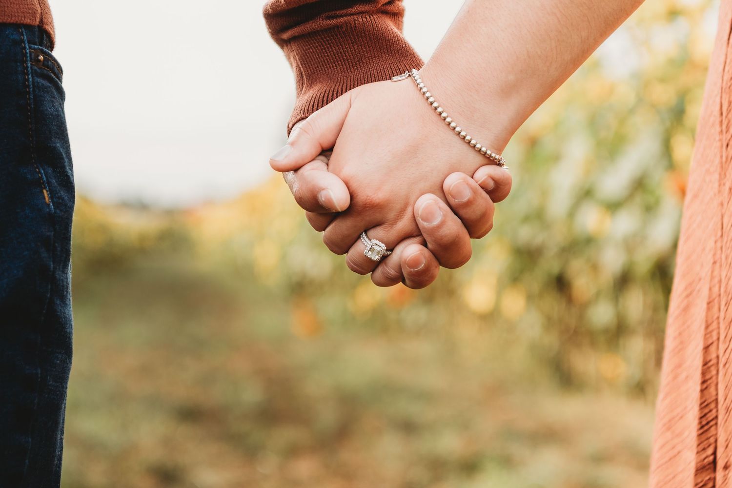 Close-up of intertwined hands against sunset background.