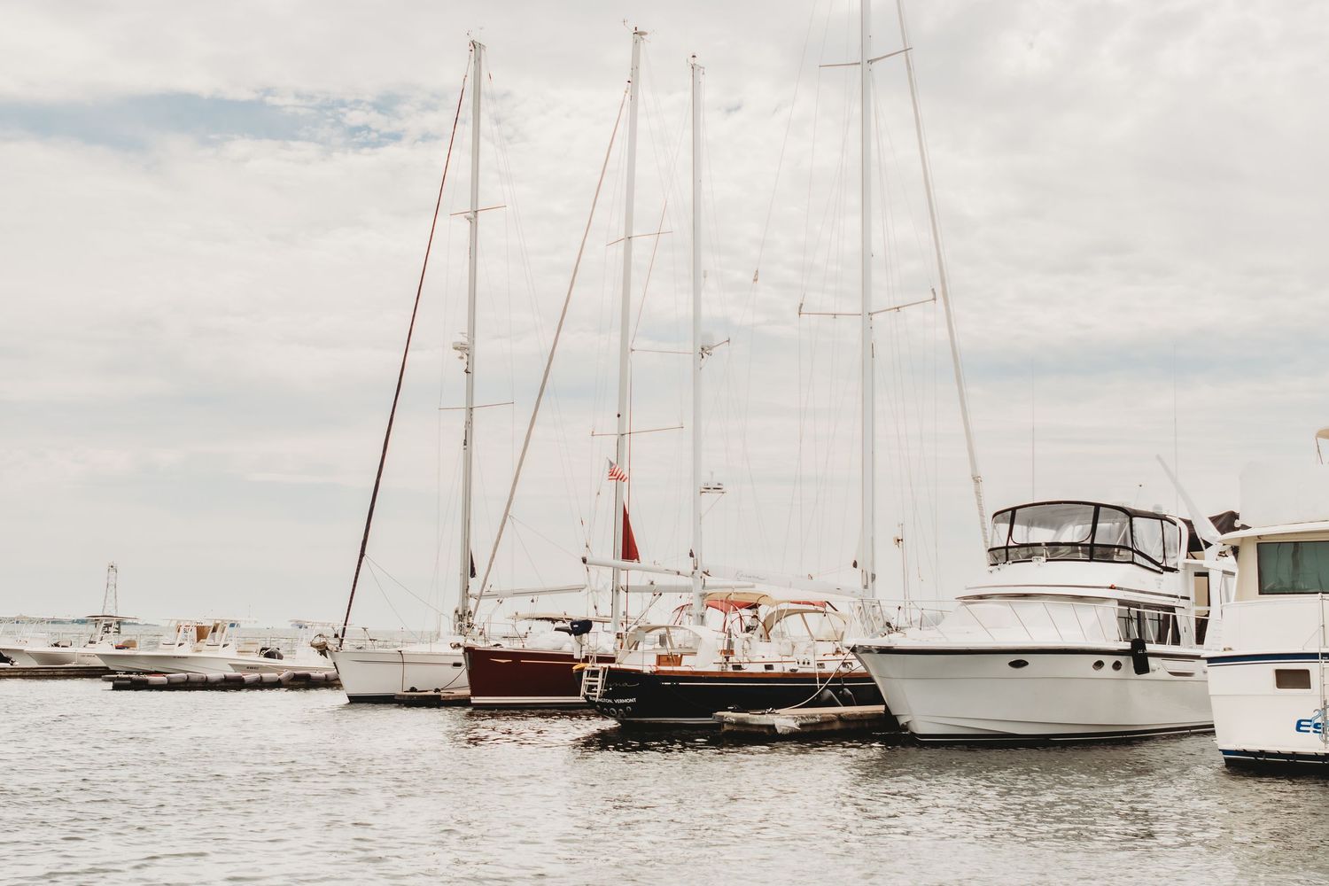 Multiple sailboats and yachts anchored in calm waters under cloudy skies.