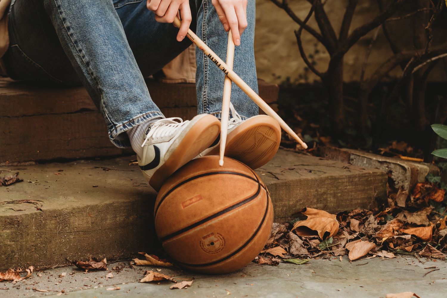 Basketball and drumstick on ground with fallen autumn leaves.