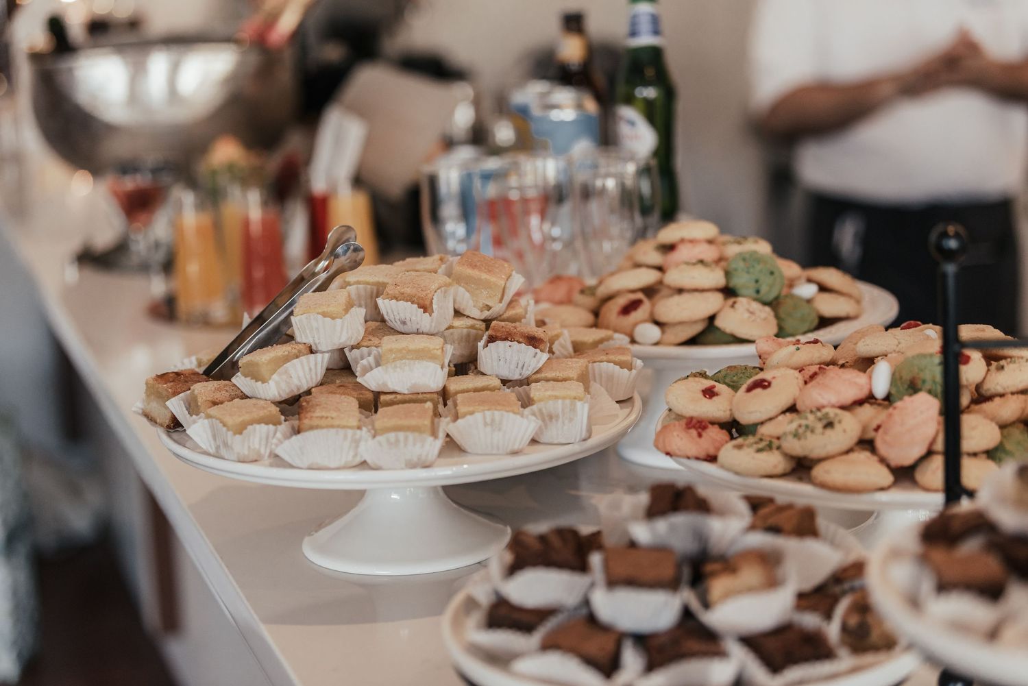 An elegant dessert display featuring various bite-sized treats arranged on white serving platters.