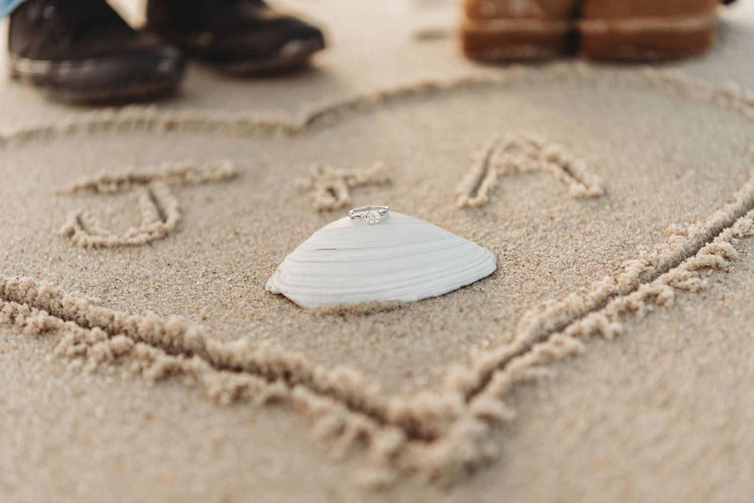 Writing in the sand at the beach with footprints visible.