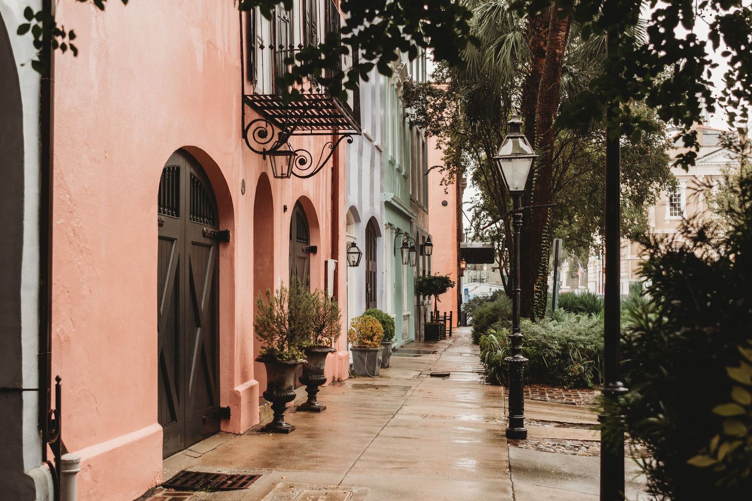 Colorful pastel buildings line a charming cobblestone street with lush greenery and a vintage lamp post.