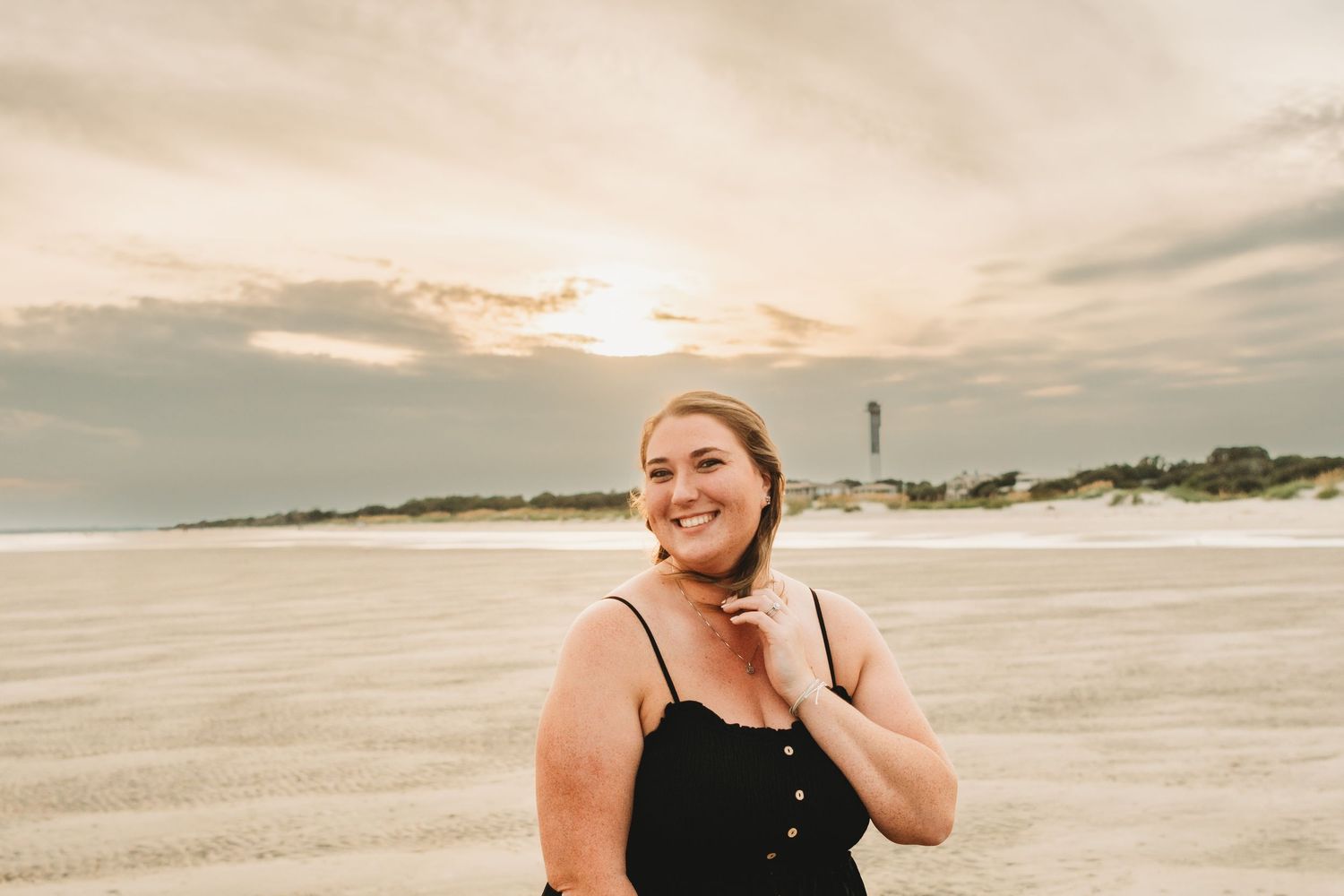 Woman enjoying sunset on a sandy beach with warm golden light and coastal views.
