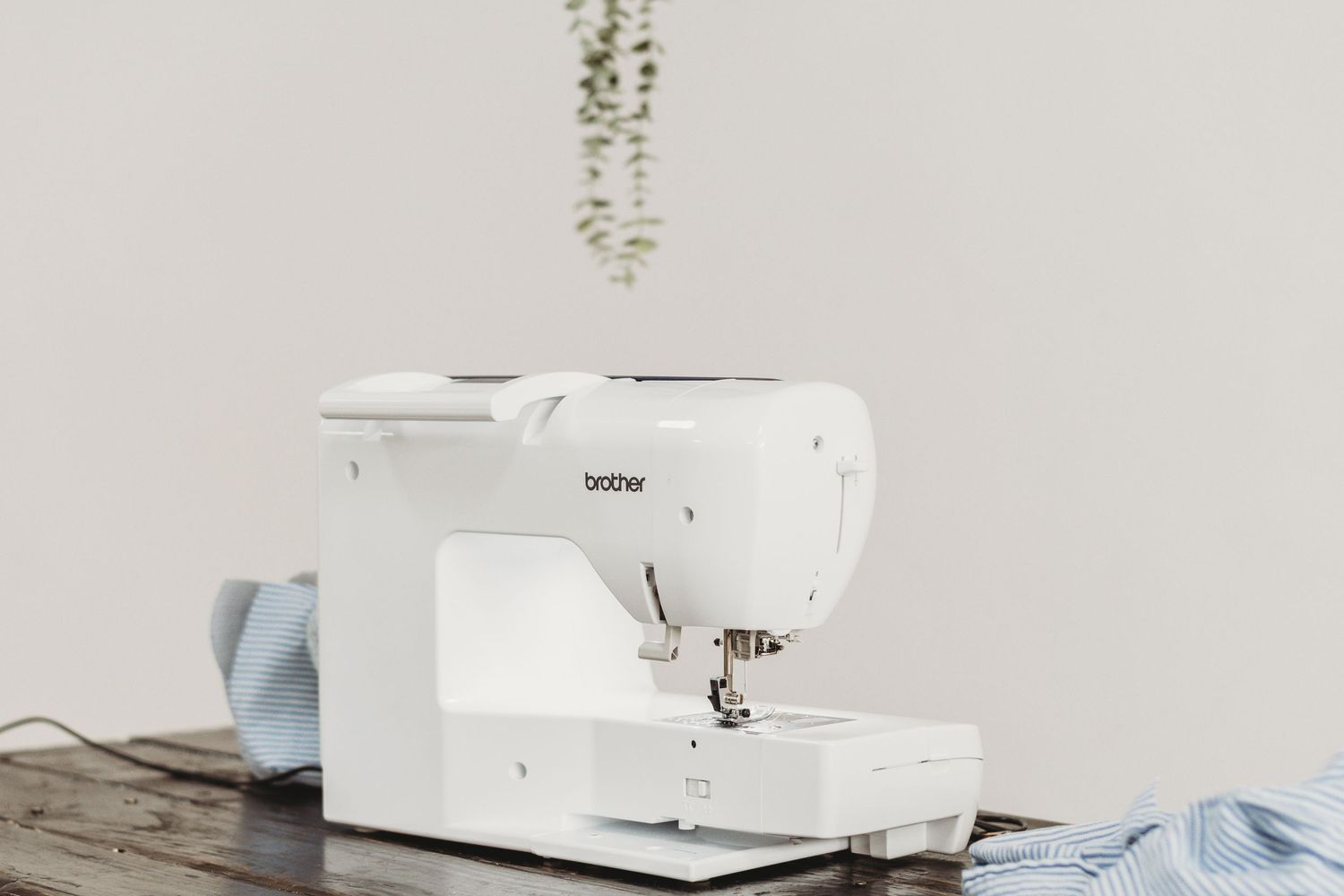 White sewing machine and craft supplies arranged on a light surface with eucalyptus sprigs.