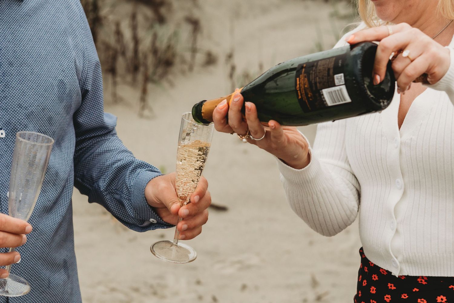 Woman pouring champagne into a flute glass on a sandy beach during an outdoor celebration.