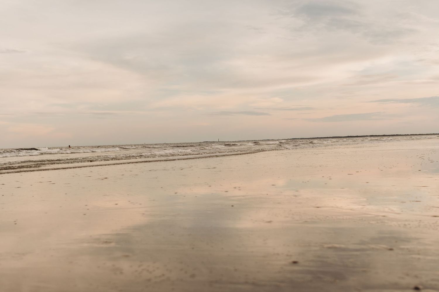 A serene panoramic view of an empty beach stretches across the horizon under cloudy skies.