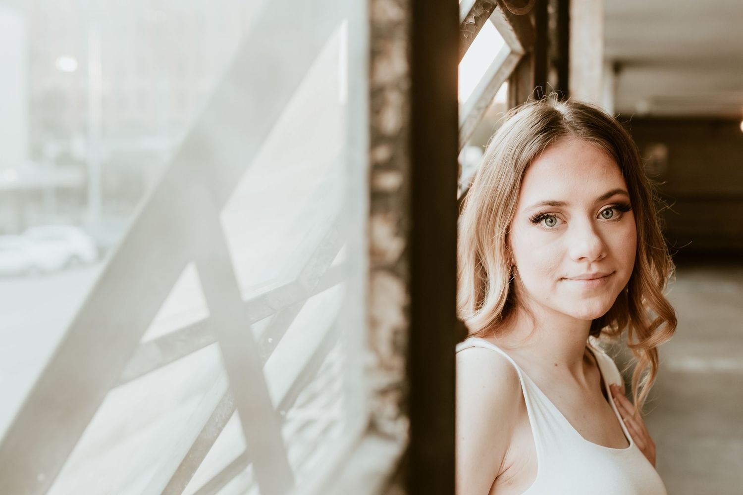 Portrait of person in white tank top near window with soft natural lighting.