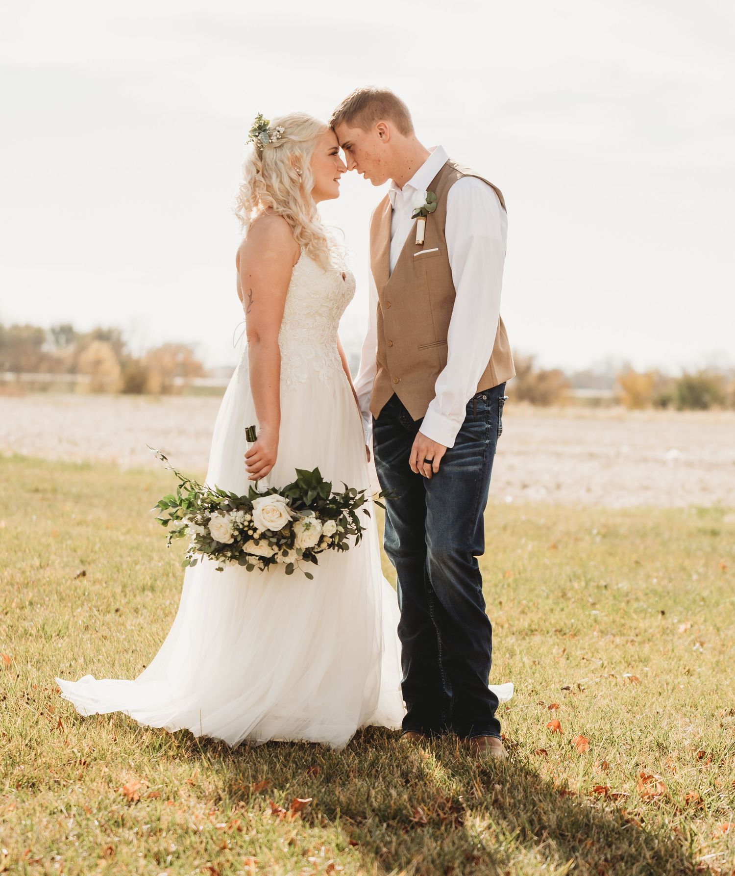 Couple in wedding attire embraces in a sunlit field during golden hour.