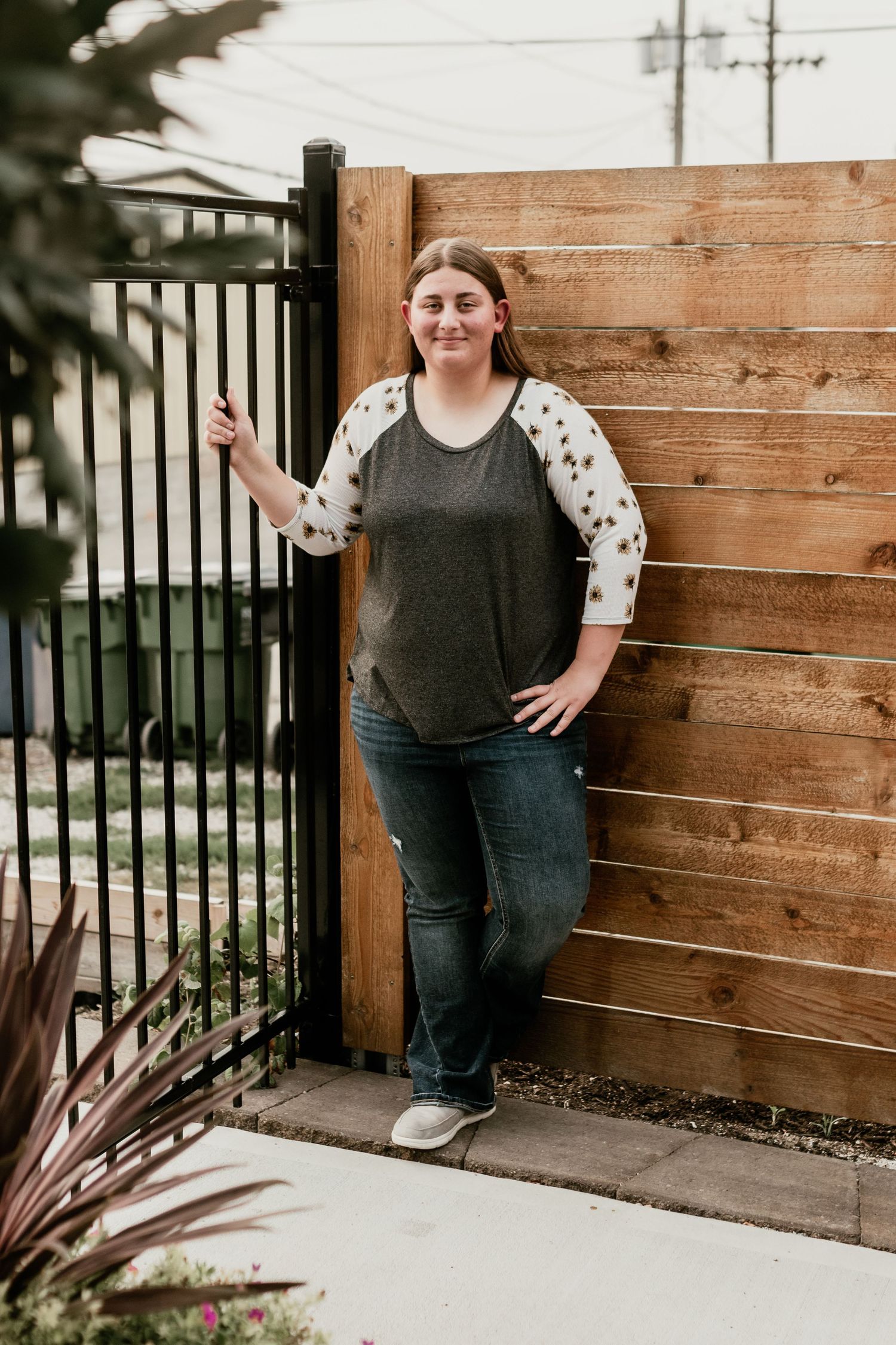 Person in casual attire poses against wooden fence backdrop.