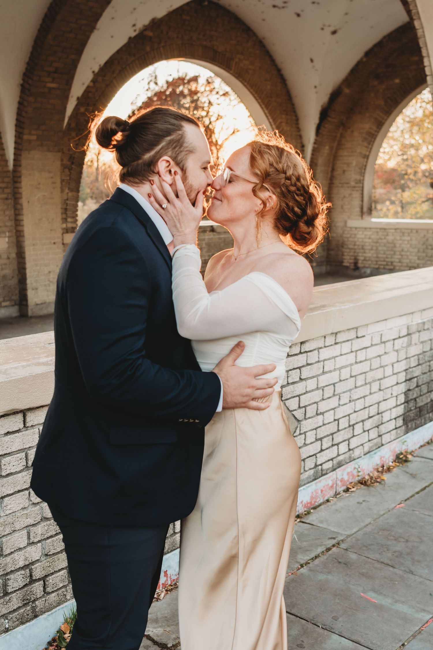 Couple sharing an intimate moment under brick archways during autumn.