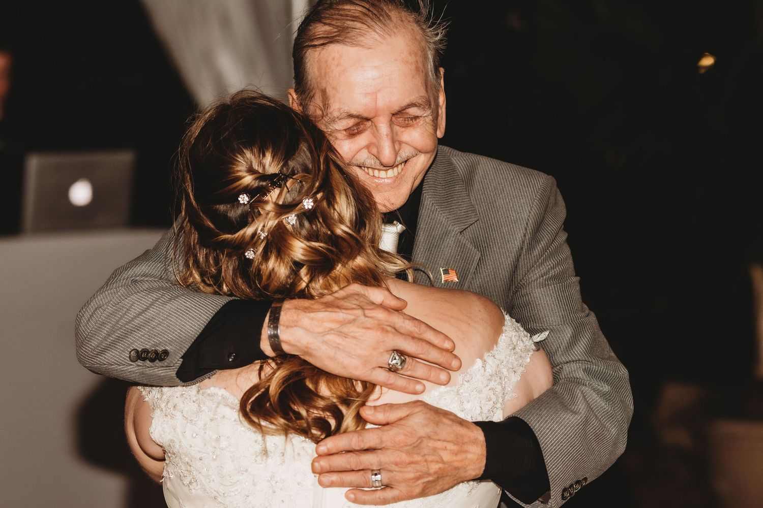 Tender embrace during wedding dance with moody dark lighting and emotional expressions.