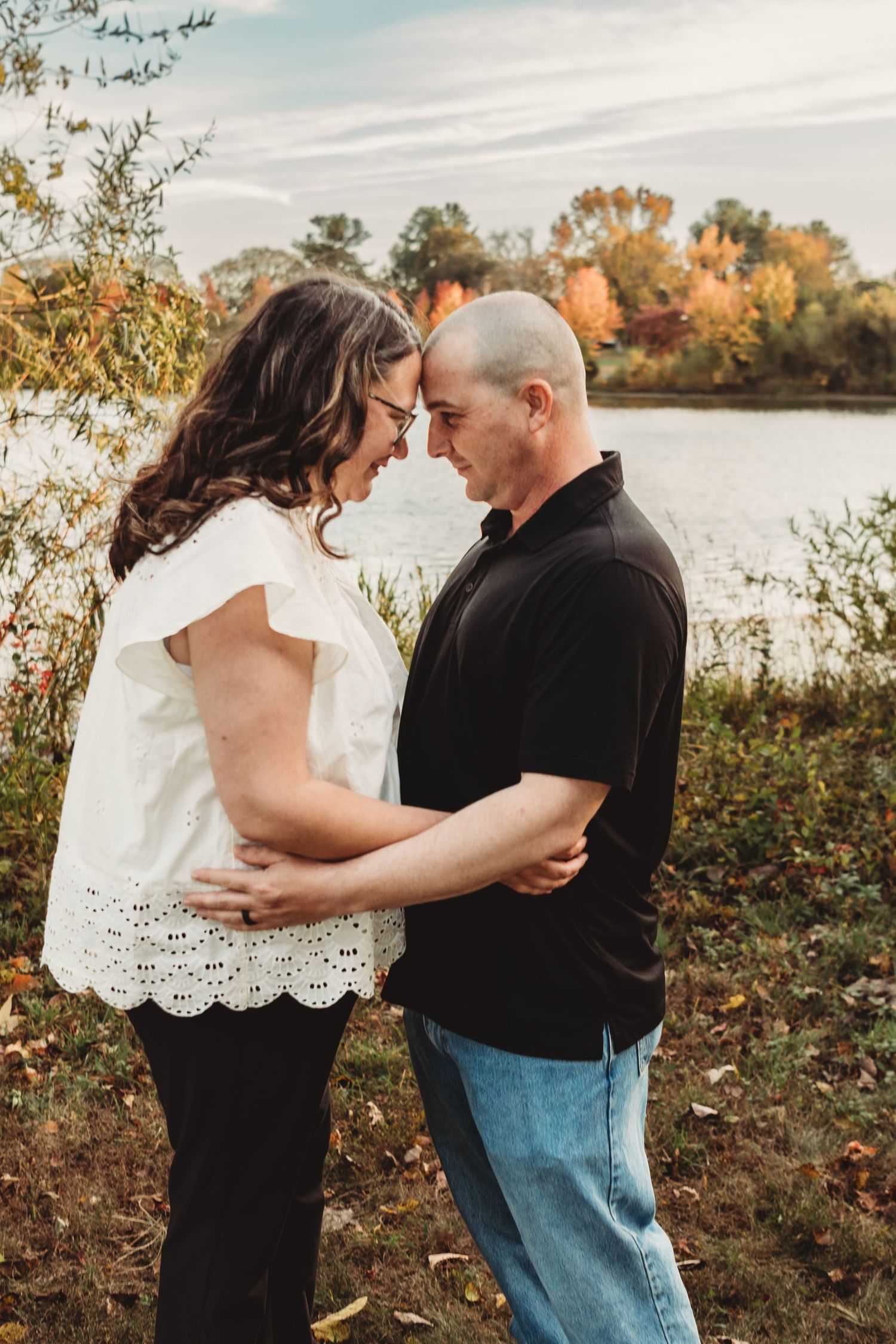 Couple in casual attire sharing intimate moments by a lakeside during sunset.