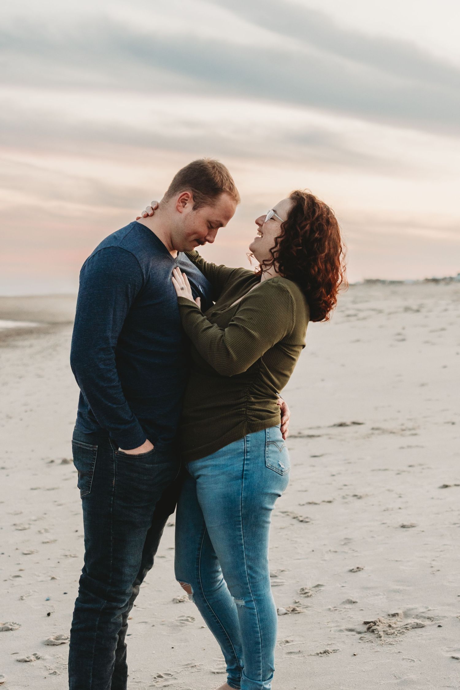 Romantic couple embracing and laughing together on sandy beach at sunset.