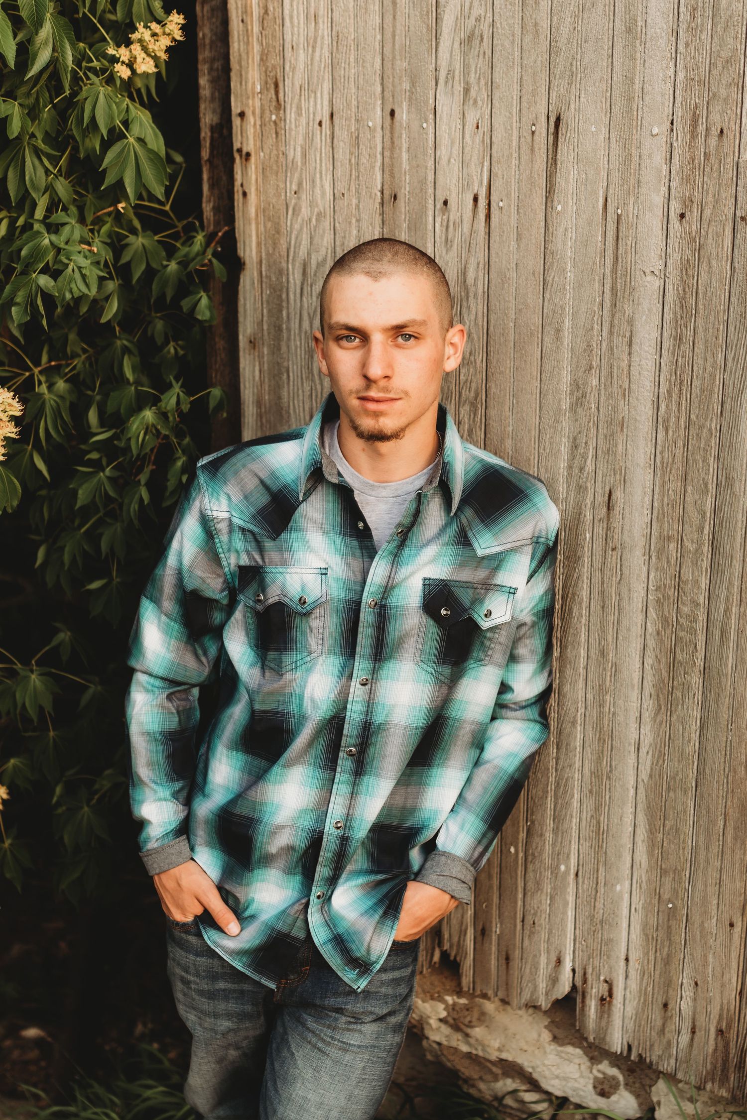 Person in teal plaid shirt poses against wooden fence backdrop.