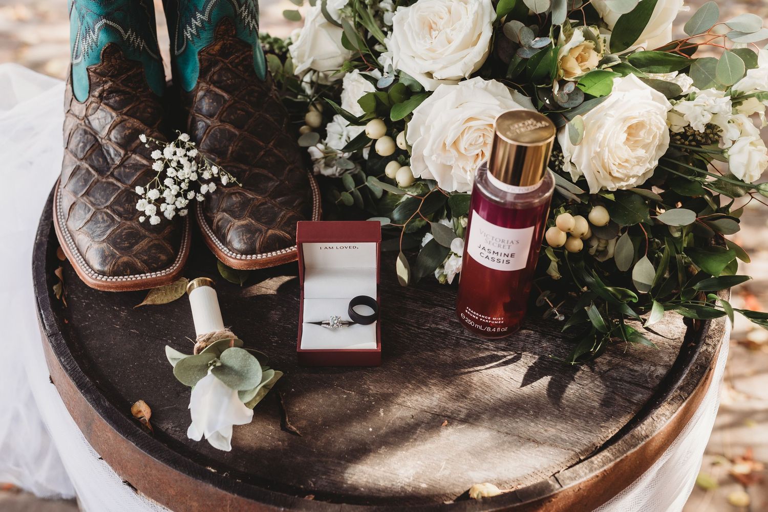 Wedding details including flowers, boots, and perfume bottles arranged on rustic wood.