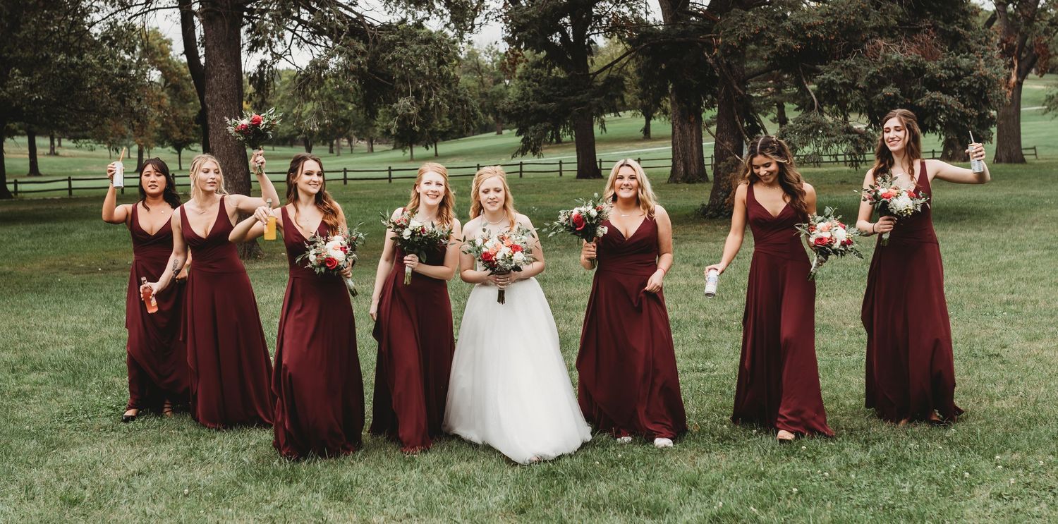 Wedding party in burgundy dresses posing together on a grassy hillside.