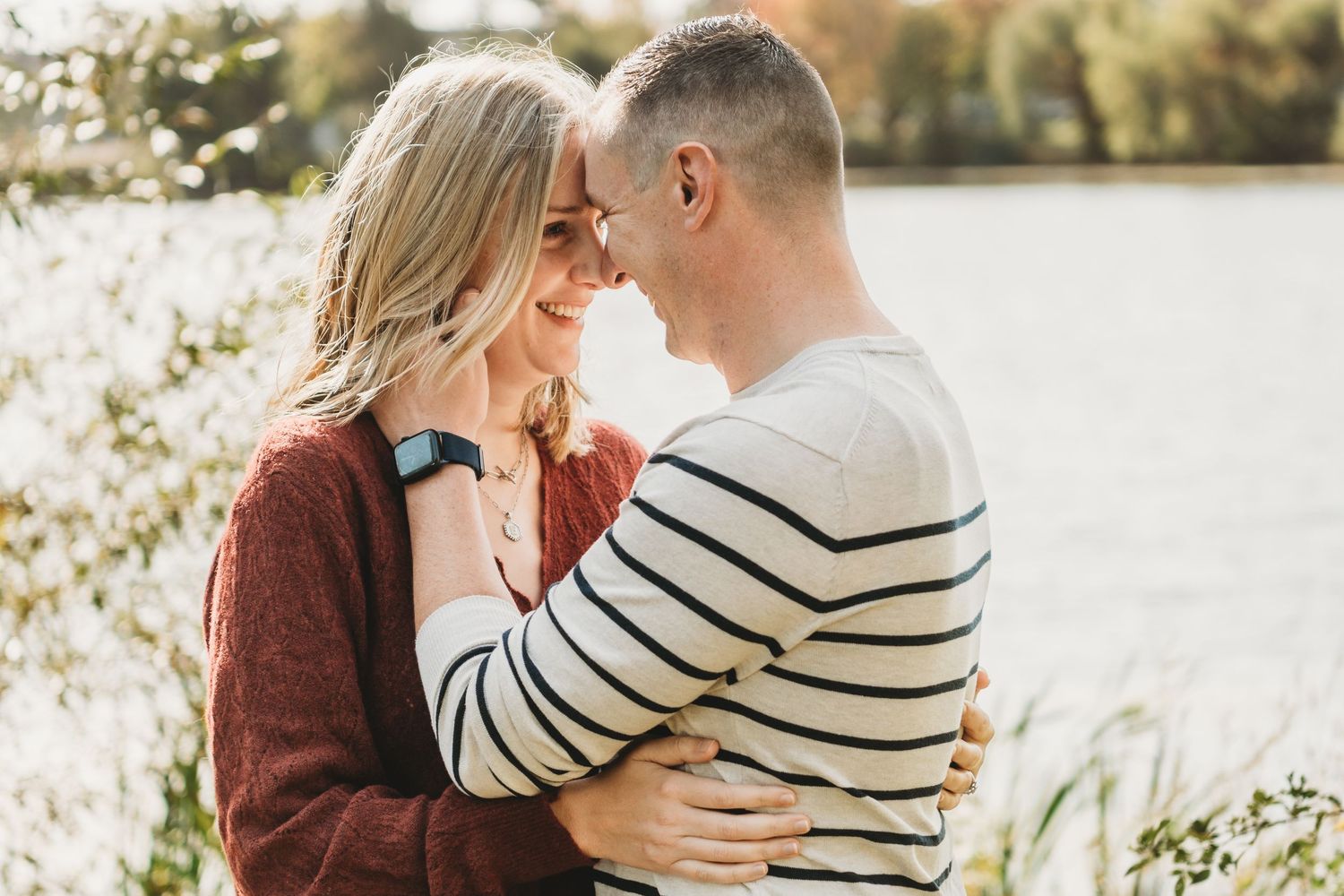 Couple in casual sweaters embracing by lake during autumn.