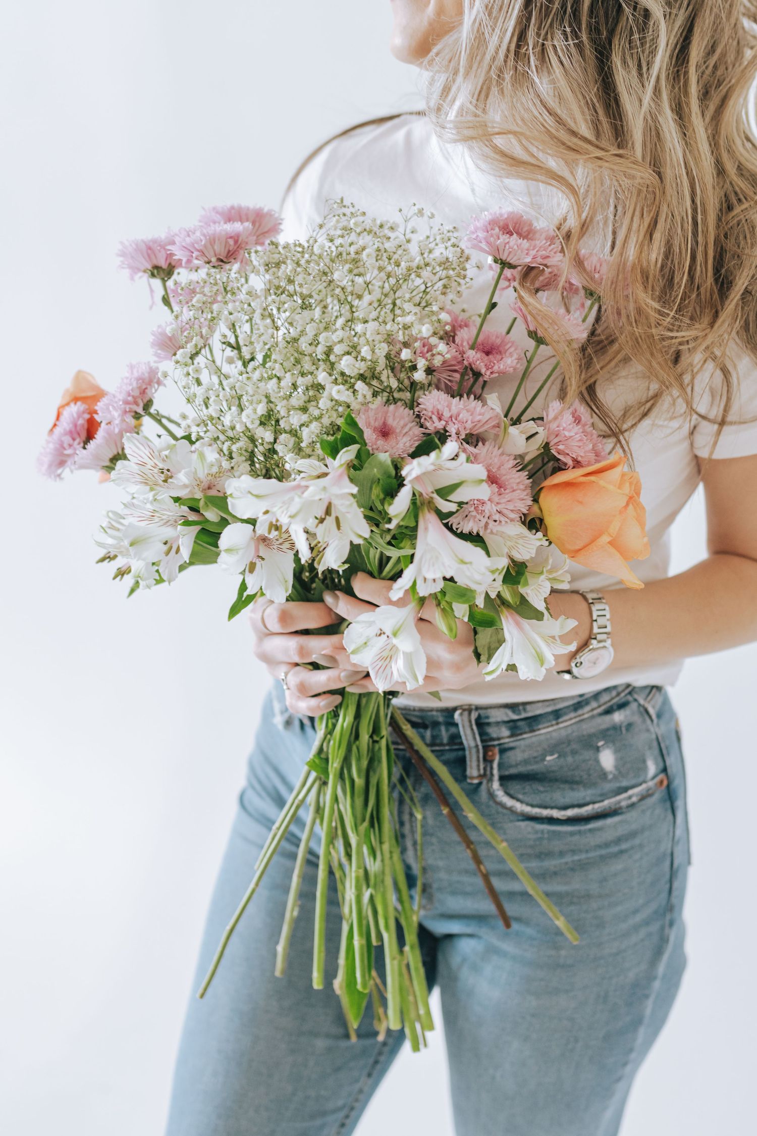 Delicate bouquet of pink and white flowers with baby's breath held against light background.