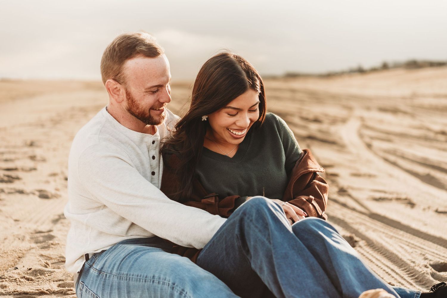 Couple sitting together on sandy beach at sunset.