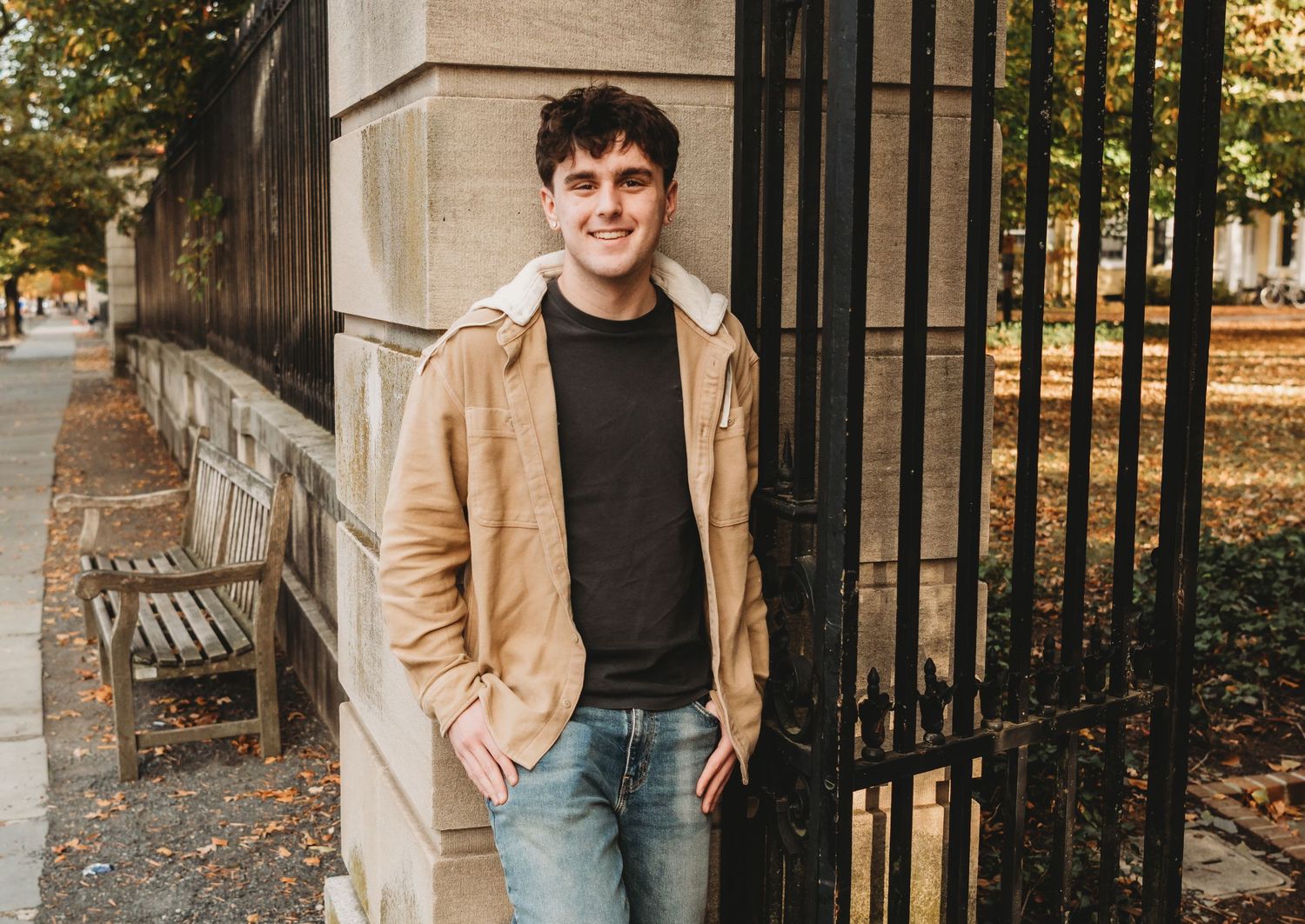 Person in casual attire standing by stone building with autumn leaves.