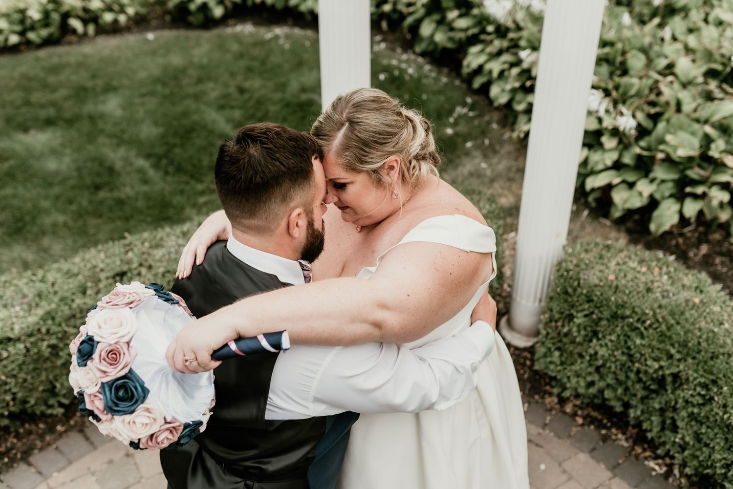 Romantic outdoor wedding scene with couple embracing under white gazebo.